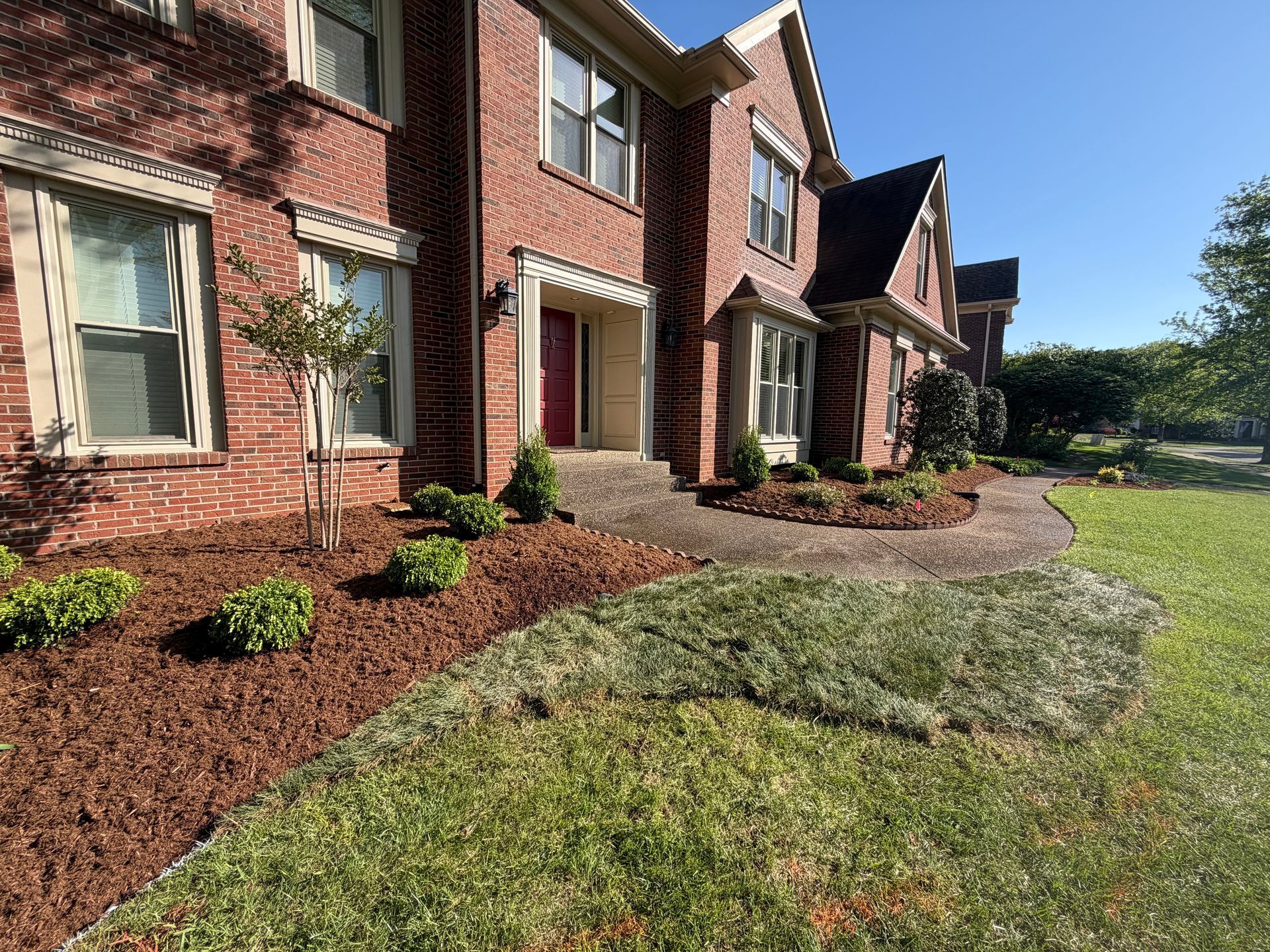Brick apartment buildings with landscaped flower beds and a grassy lawn on a sunny day
