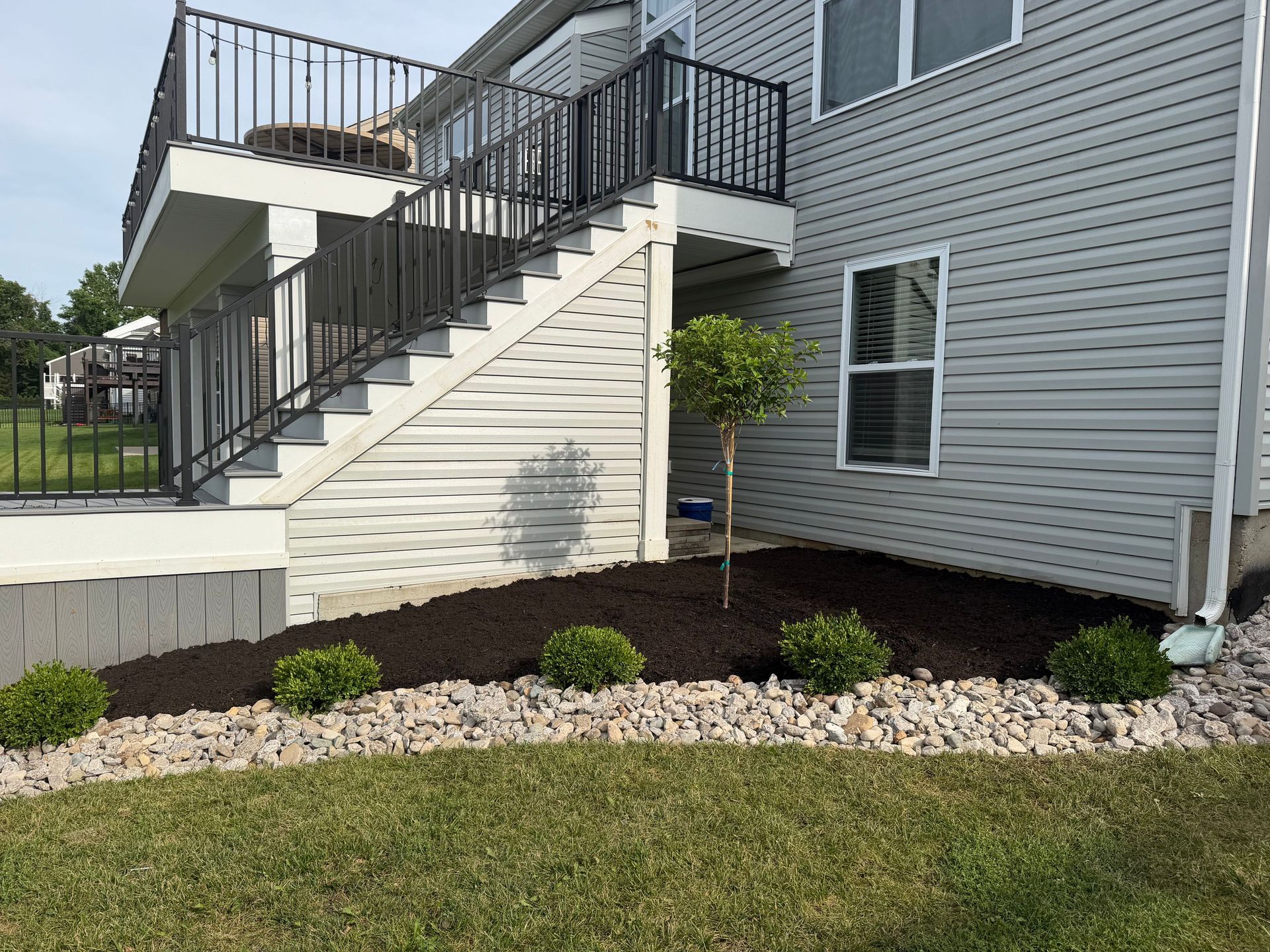 Apartment building exterior with white staircase, black railing, and landscaped rocks and grass