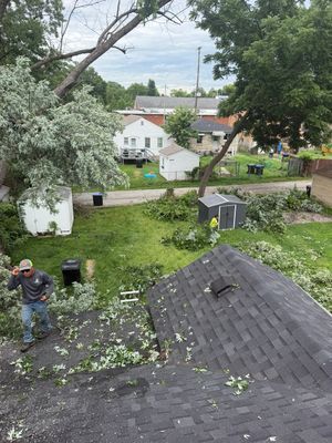 Backyard after storm damage, with fallen branches, roof shingles, and a worker clearing debris.