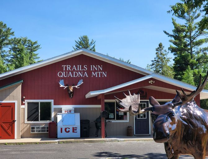 The front view of The Trails Inn Quadna Mountain Motel office. An image of the front office of The Trails Inn Quadna Mountain Motel with a moose statue.
