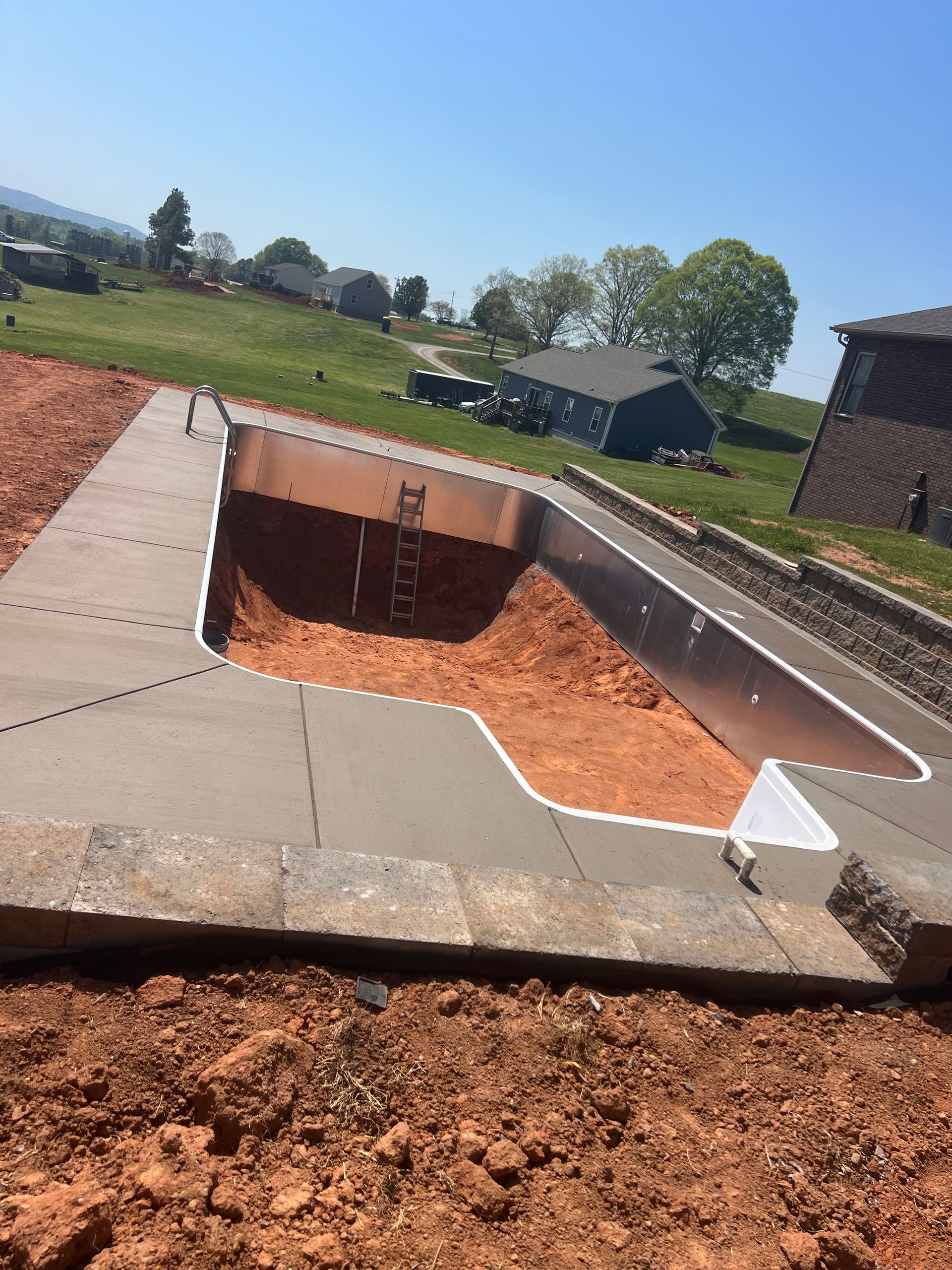 Newly constructed swimming pool with concrete edges, on sloped terrain, blue sky.