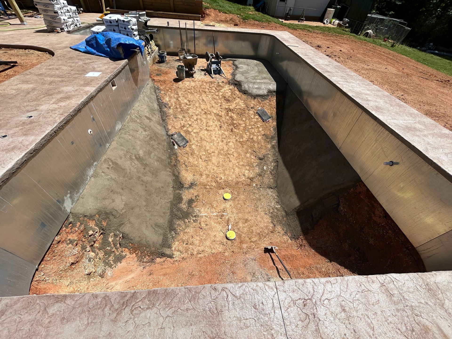 A newly constructed swimming pool basin; brown earth base with gray walls, surrounded by concrete coping.