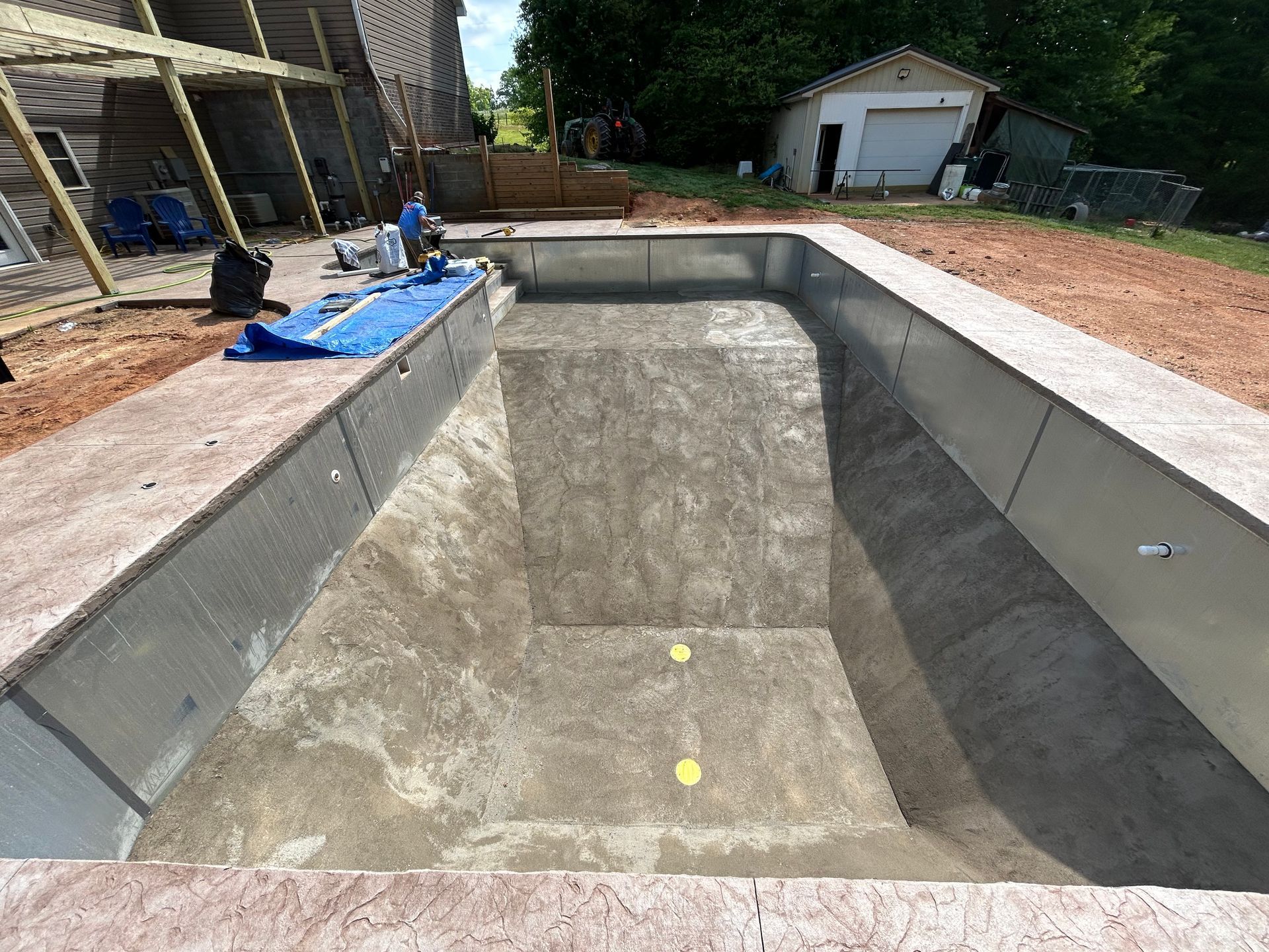 Empty rectangular swimming pool under construction, concrete walls and surround, blue tarp, sunny day.