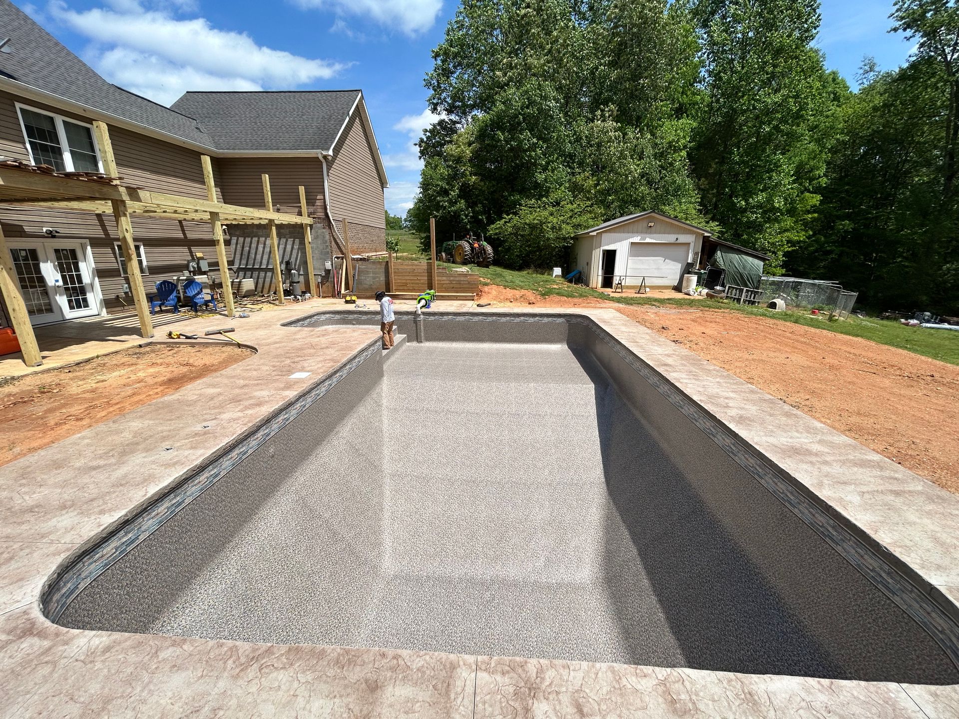 Empty rectangular swimming pool under construction, next to a house on a sunny day.