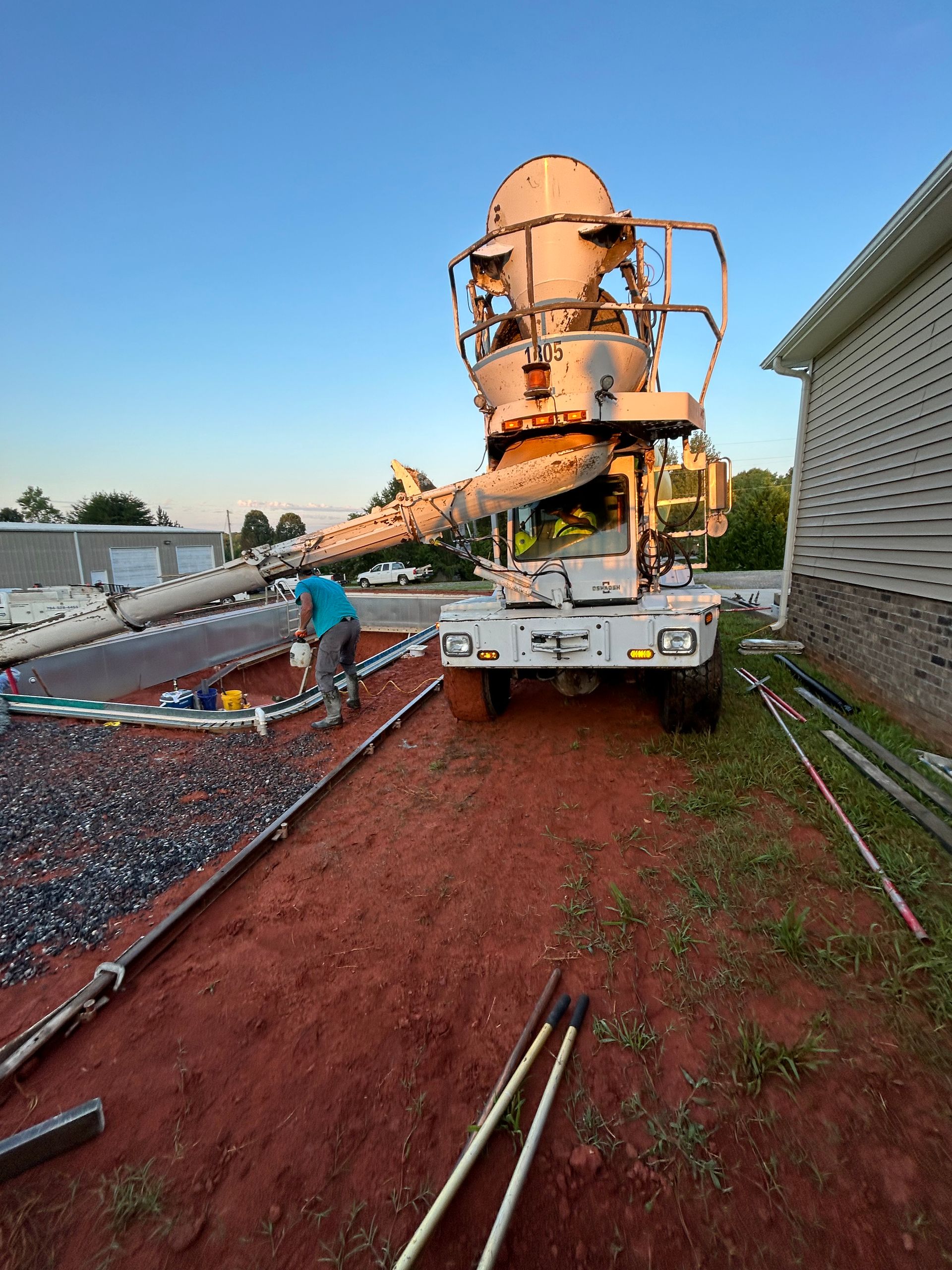 Concrete truck pouring concrete on a construction site. A worker guides the pouring, setting is outdoors with evening light.