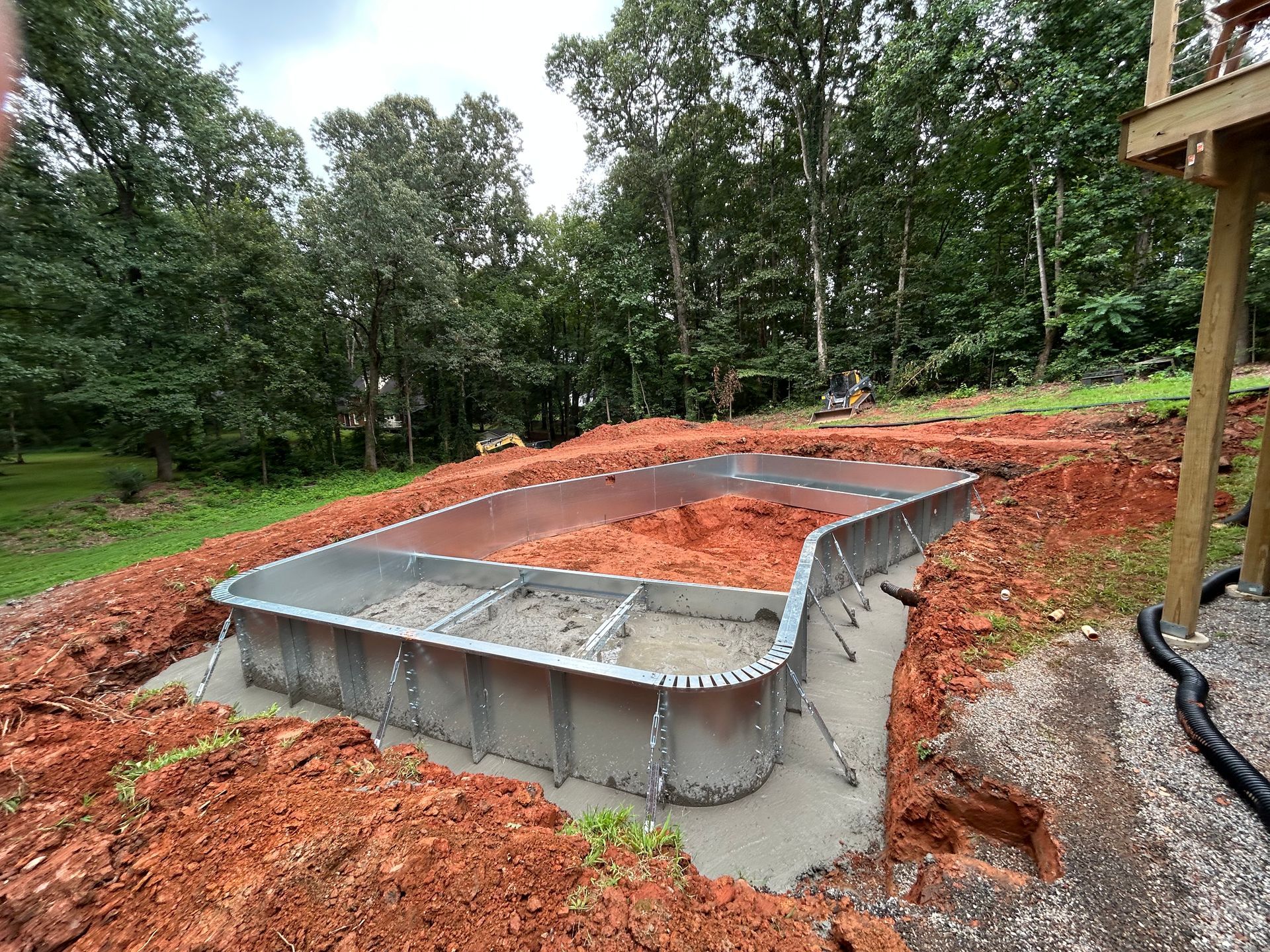 Pool under construction in a yard with dirt and trees in the background.