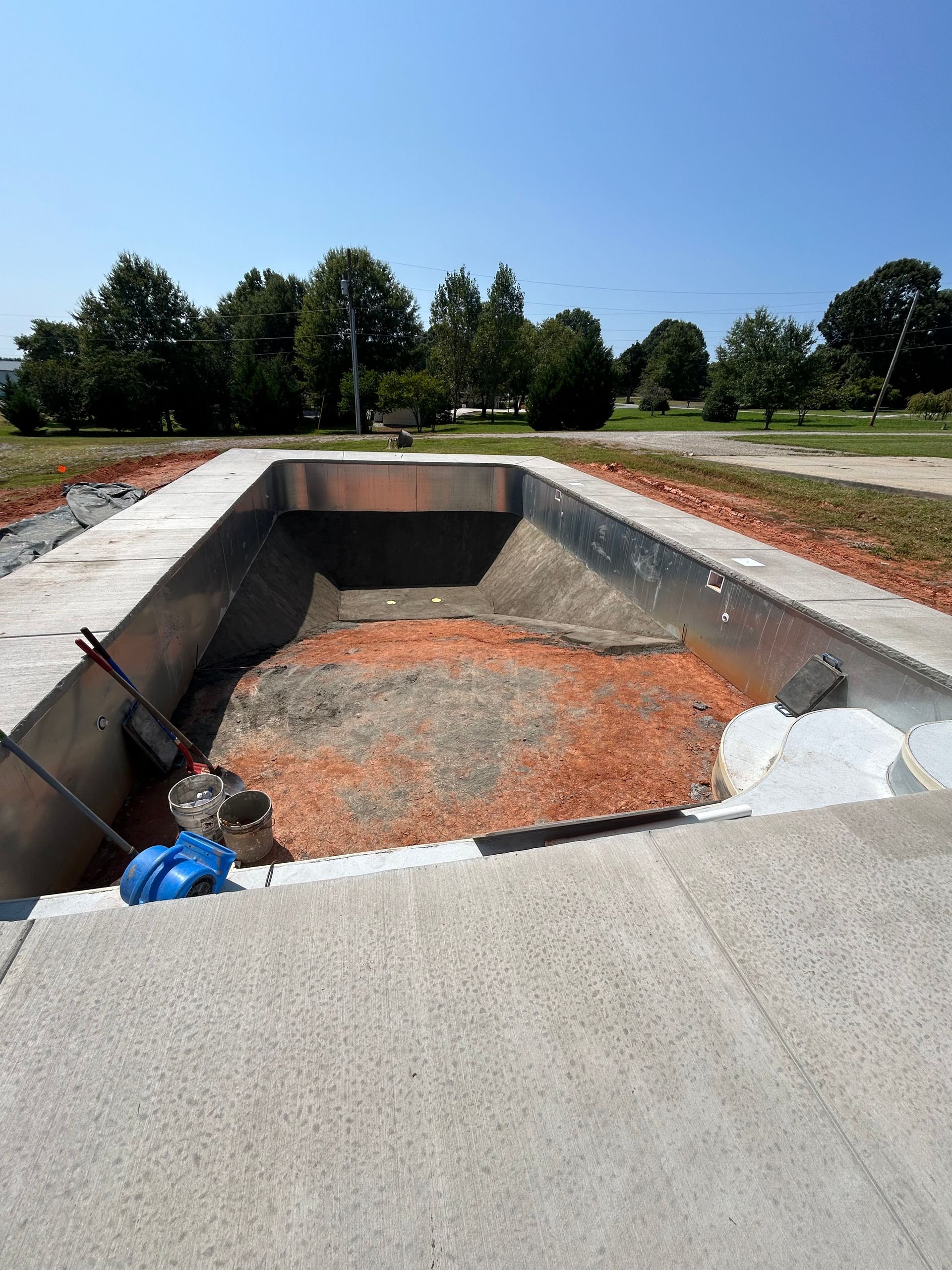 Empty rectangular concrete pit, possibly for swimming or landscaping, in an outdoor setting on a sunny day.