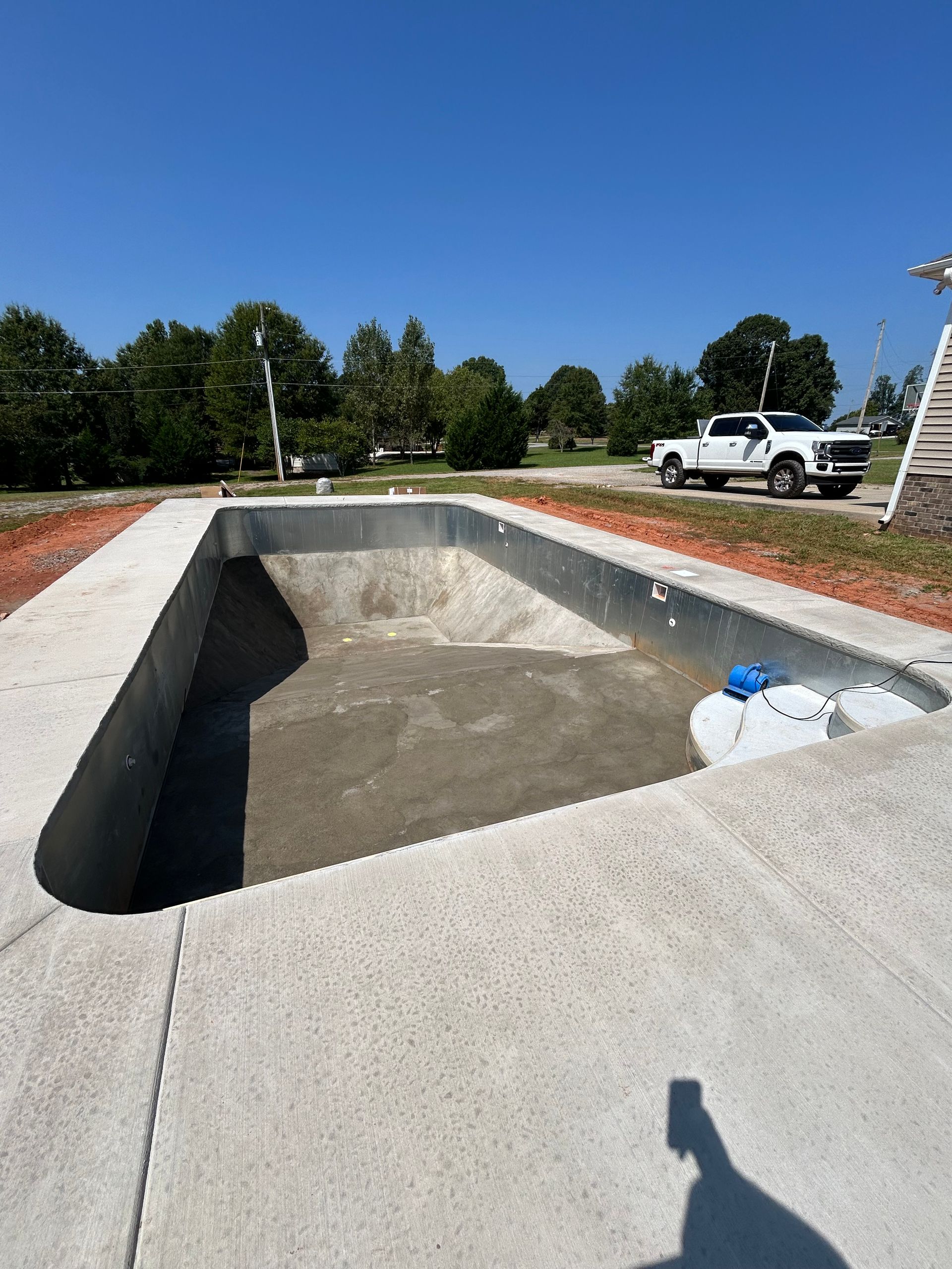 Empty rectangular pool under construction with surrounding concrete, white truck visible in the background.