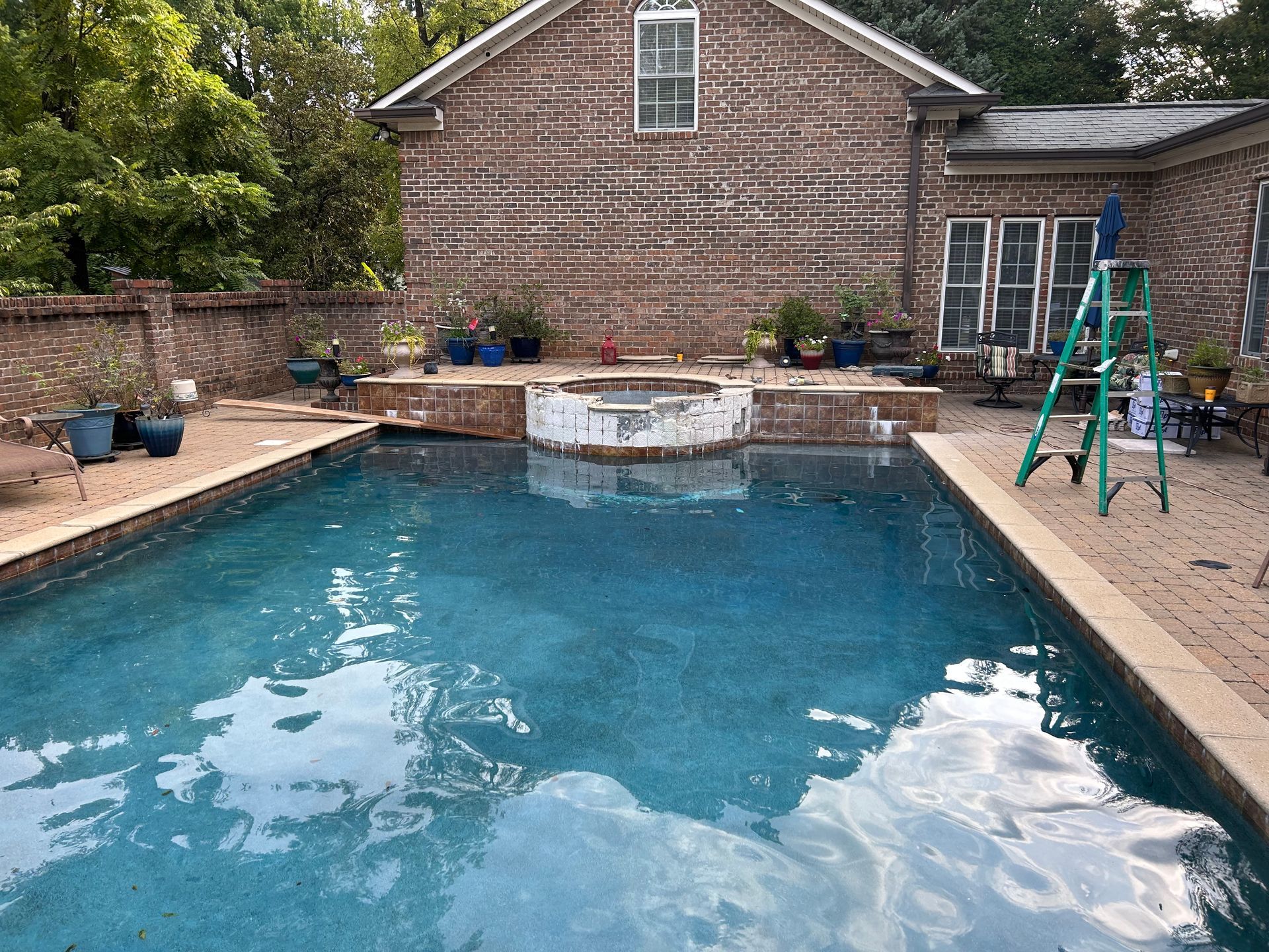 A rectangular swimming pool surrounded by brick patio, with a brick home in the background.