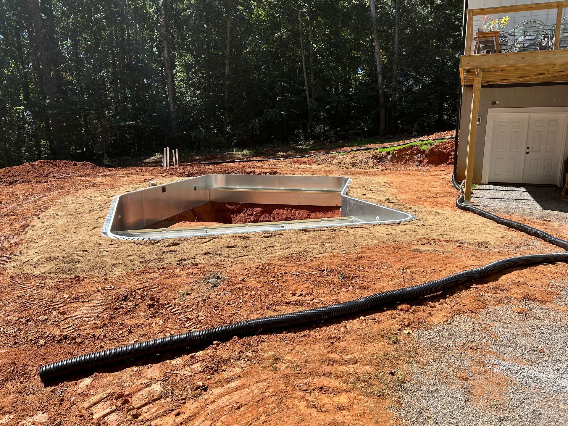 Construction site with a concrete pool foundation, dirt, and black drainage pipe.