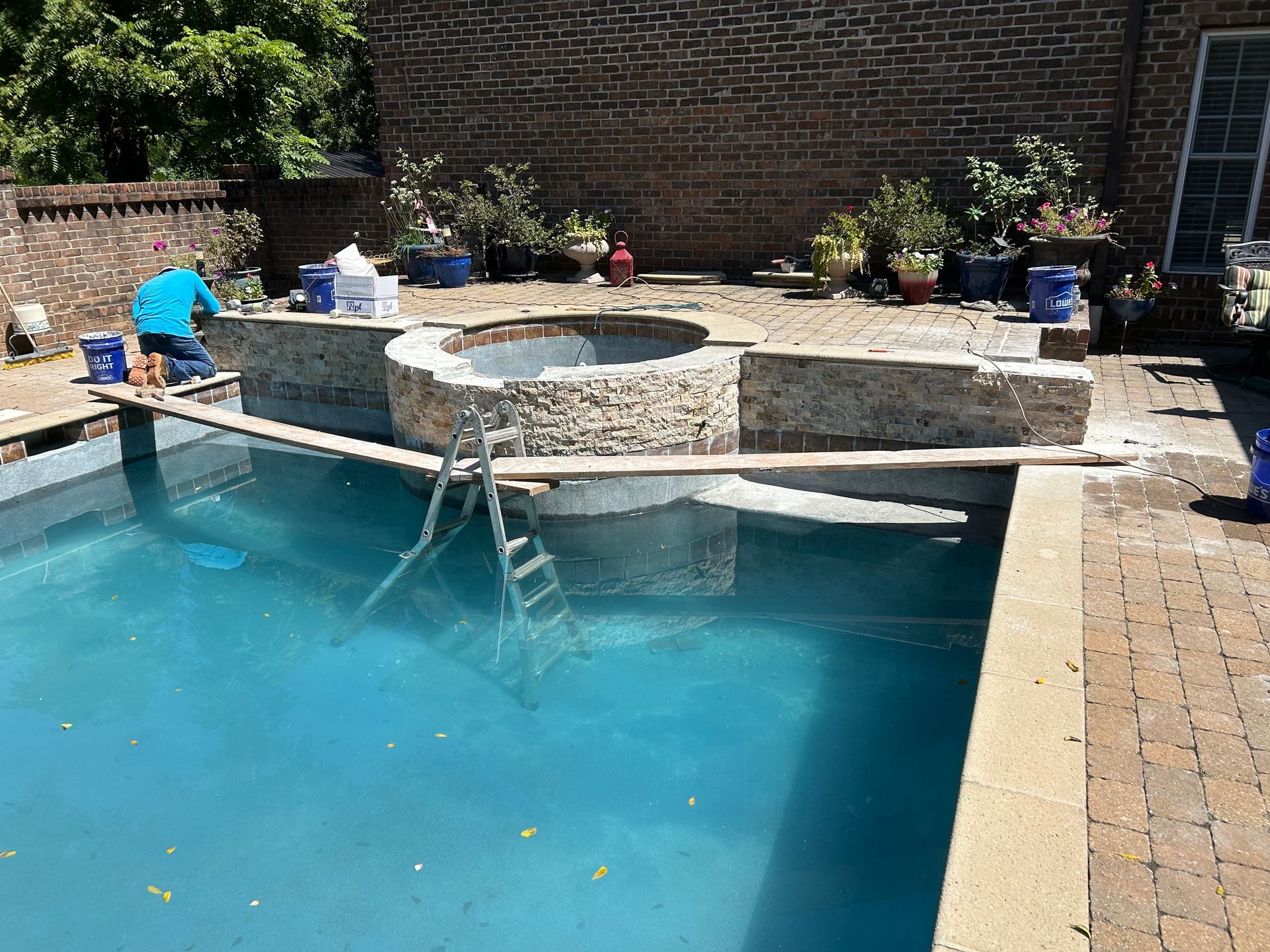 Aerial view of a rectangular swimming pool with a brick house, gazebo, and black fence.
