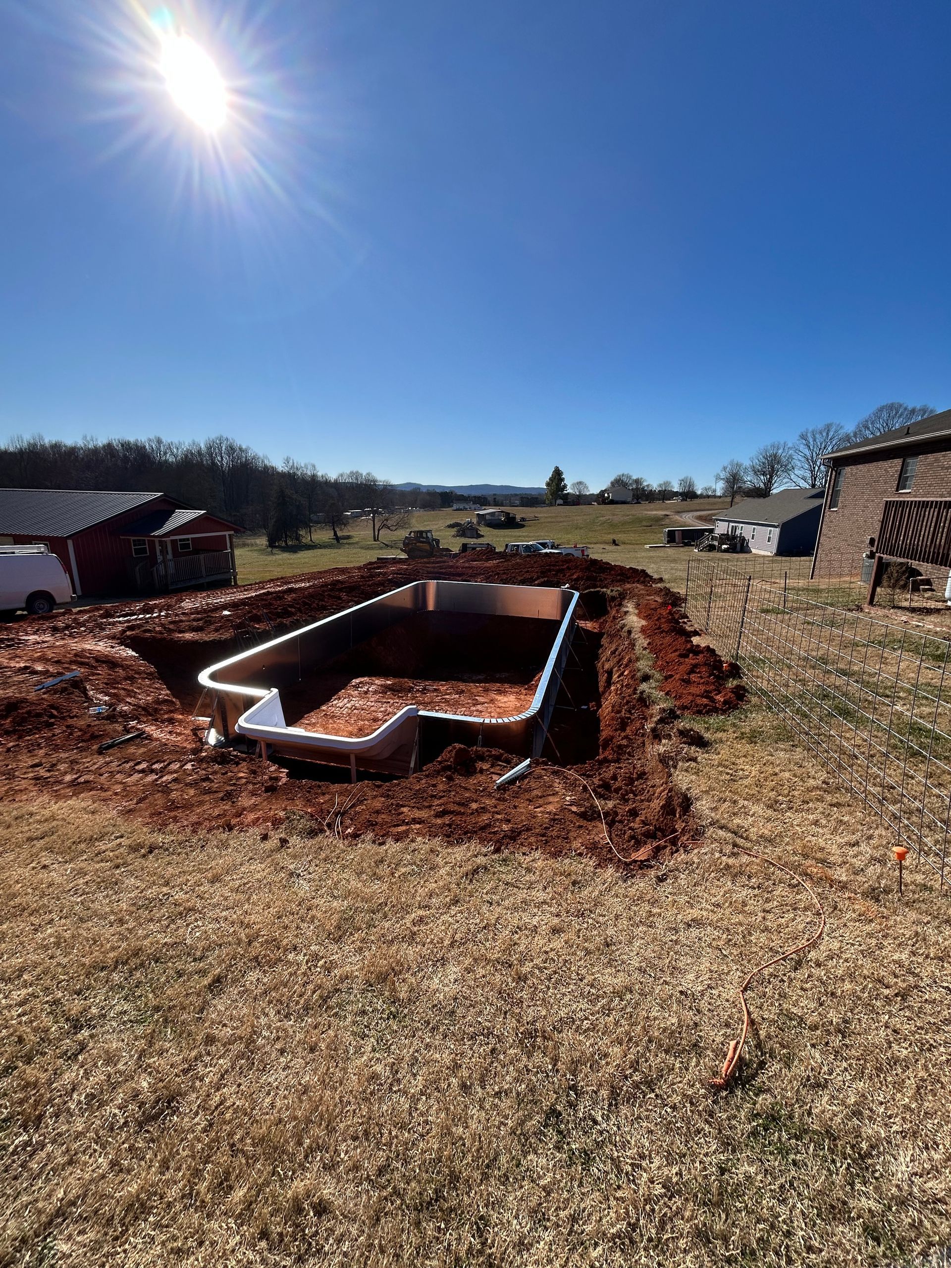 Empty pool under construction on a sunny day. Brown dirt surrounds the pool. Blue sky in the background.