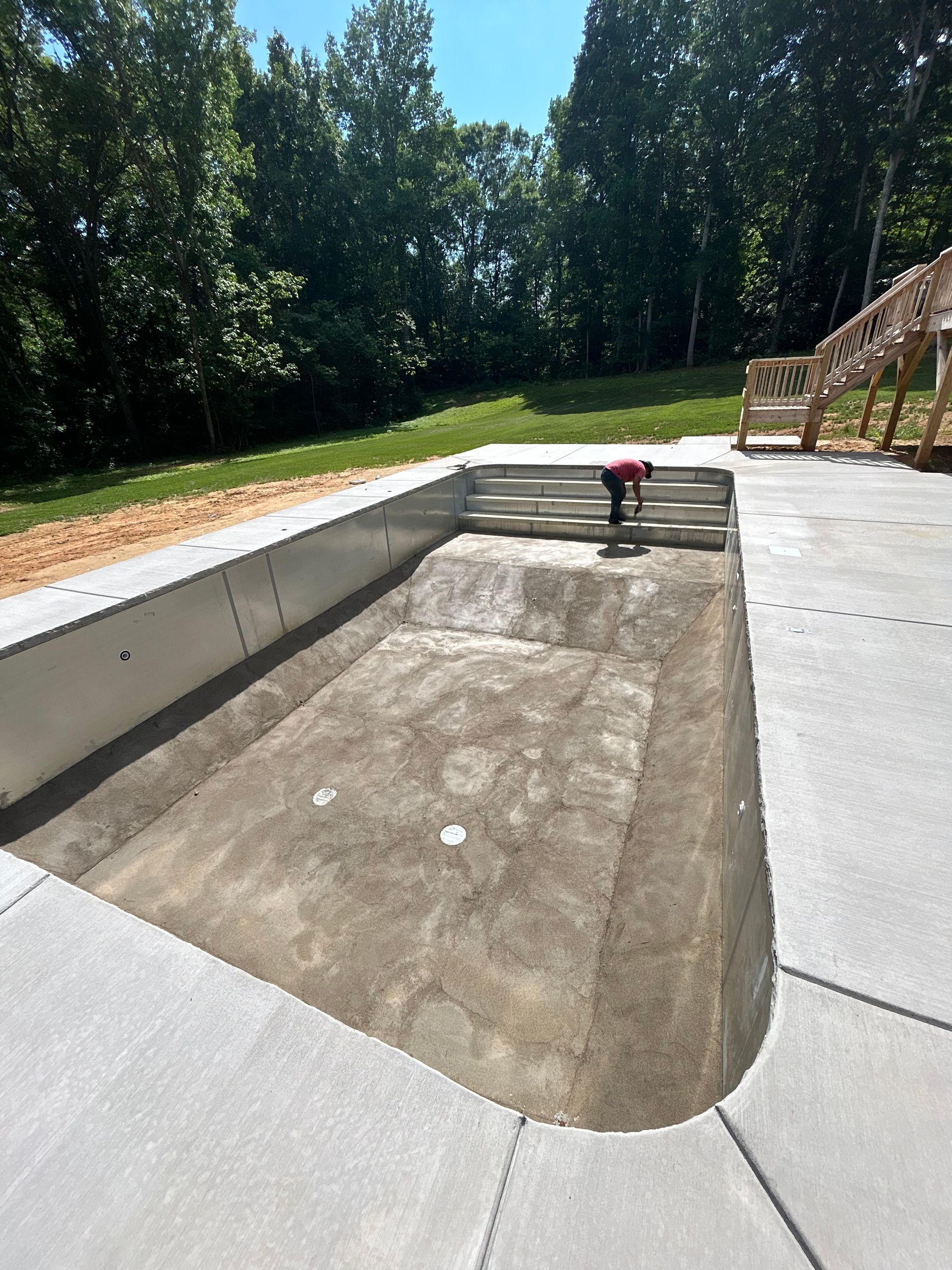 Empty concrete swimming pool under construction outdoors, surrounded by concrete deck.