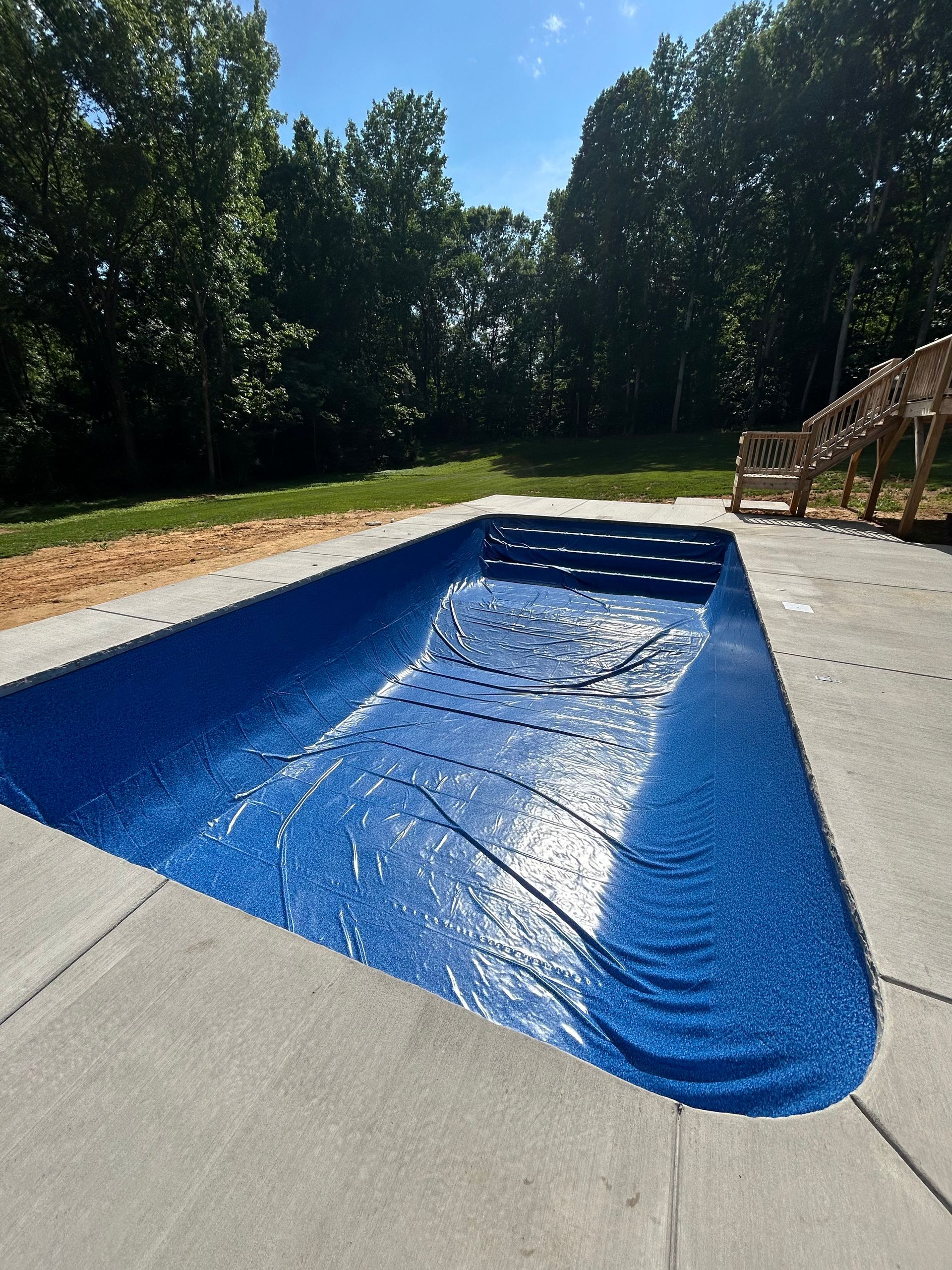 Blue swimming pool with a partially covered surface, surrounded by concrete and grass, under a bright sky.
