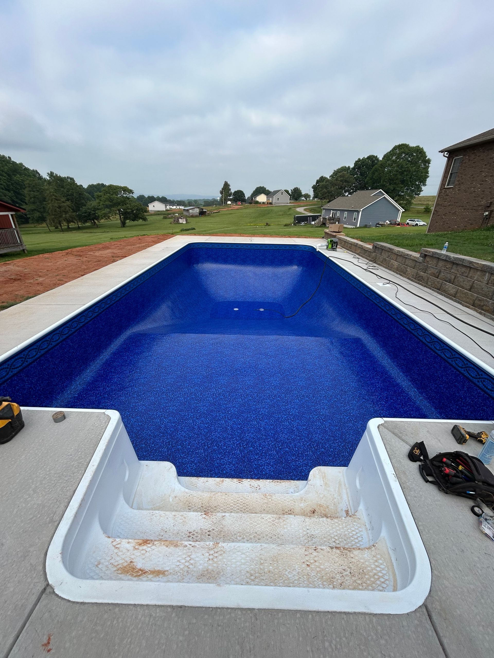 Empty rectangular pool with a blue tiled interior and white steps. Concrete patio around pool.