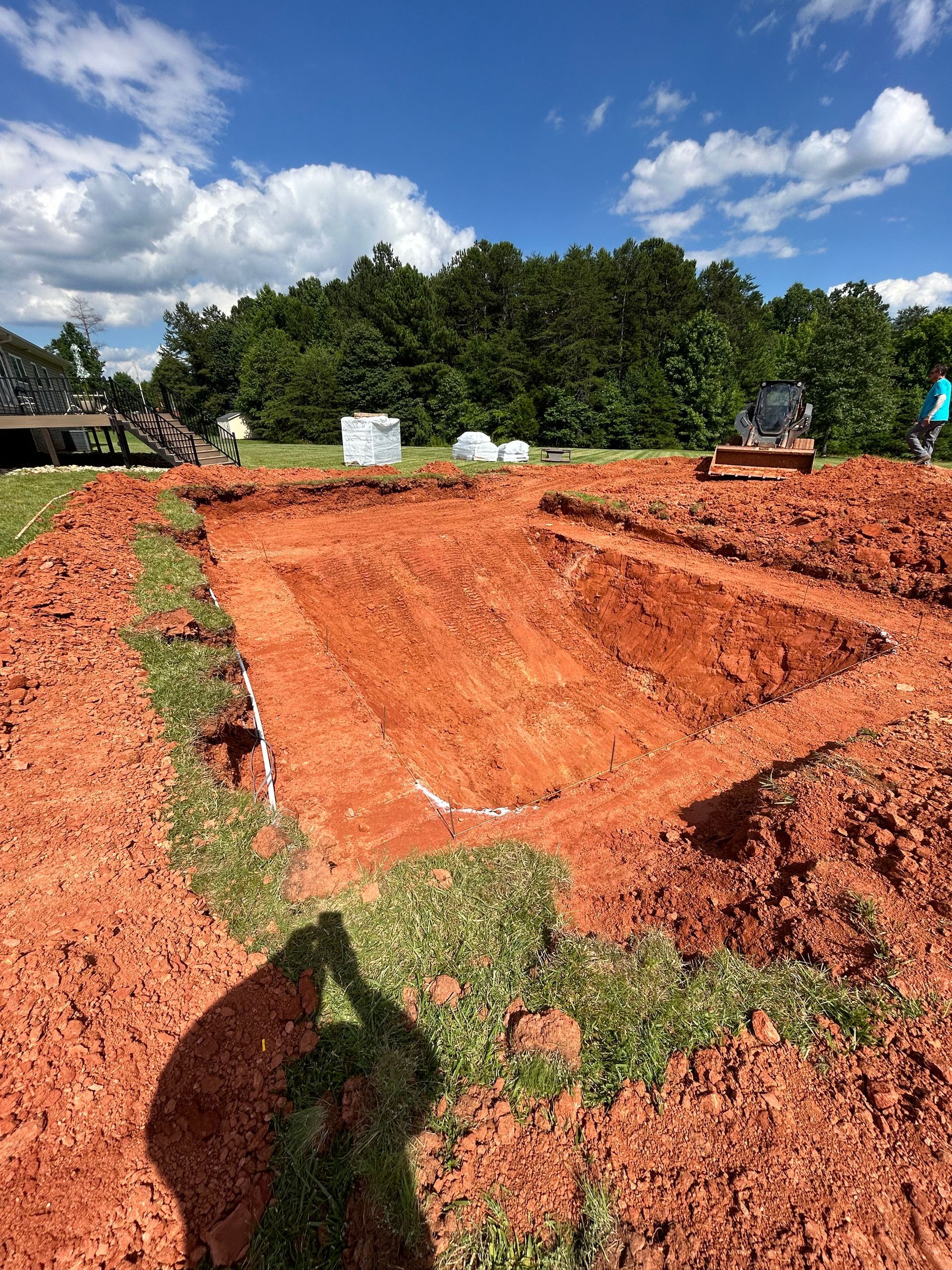Excavated red soil for construction, with grass border and trees in the background under a blue sky.