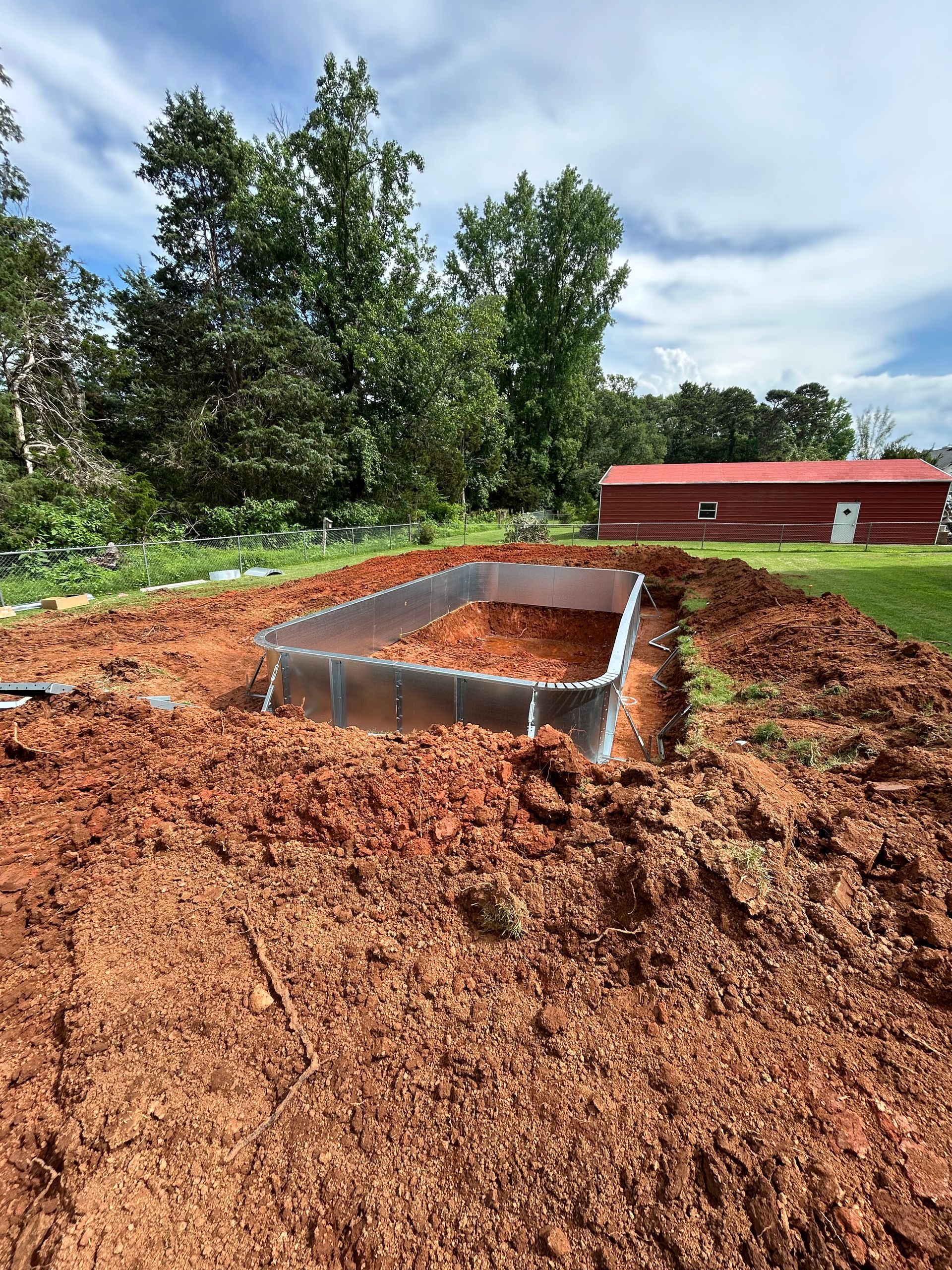 A metal-edged raised garden bed is surrounded by red mulch in a yard with a red building in the background.