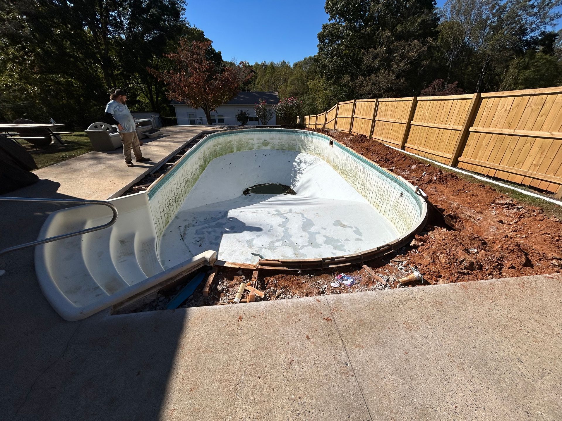 Empty pool with a person, next to a new wooden fence on a sunny day.