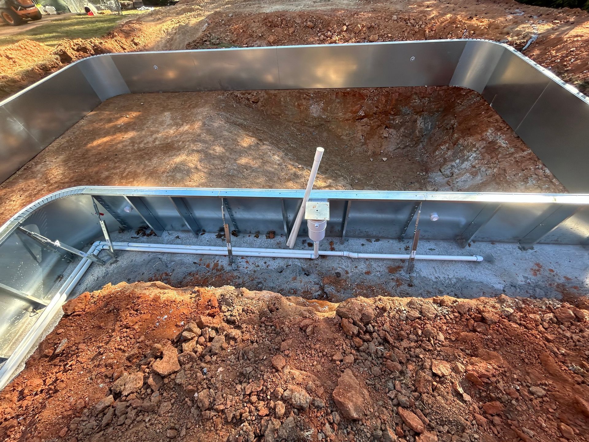 Metal pool frame in dirt, with PVC pipes and vertical support. Sunny outdoor setting.