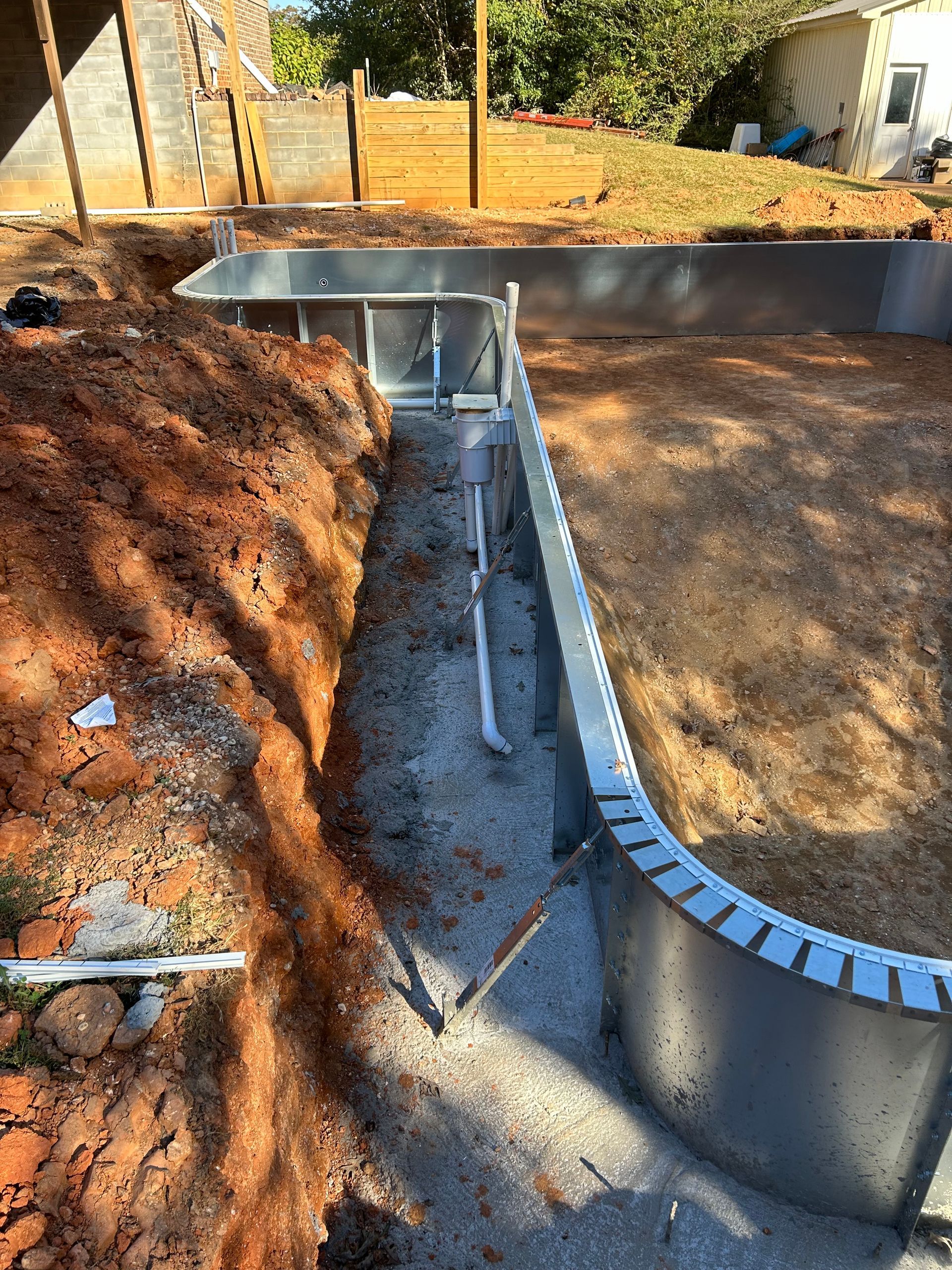 Pool construction site with metal pool frame, trenches, and dirt.