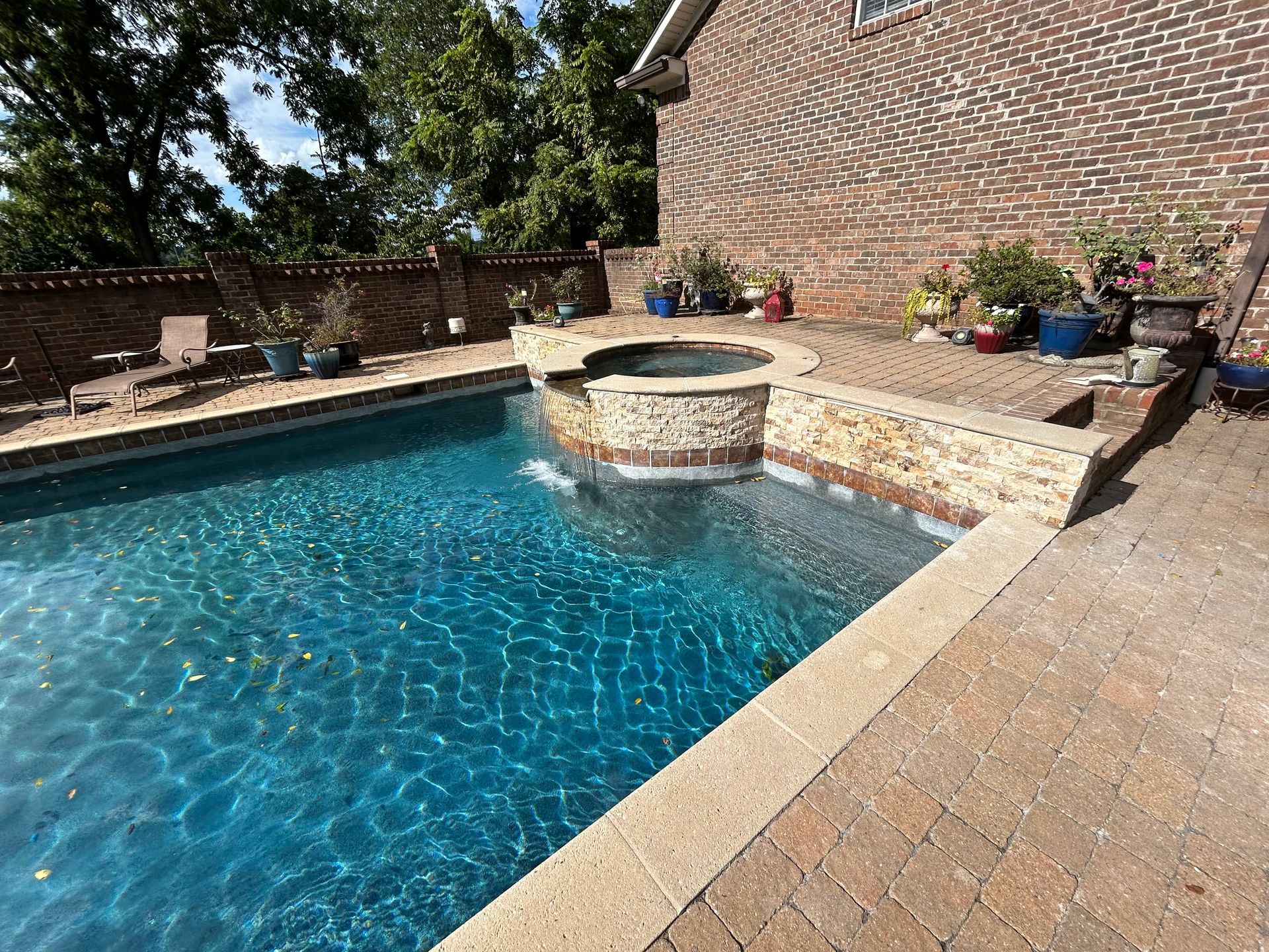 Swimming pool with attached hot tub, surrounded by brick patio and a brick wall.