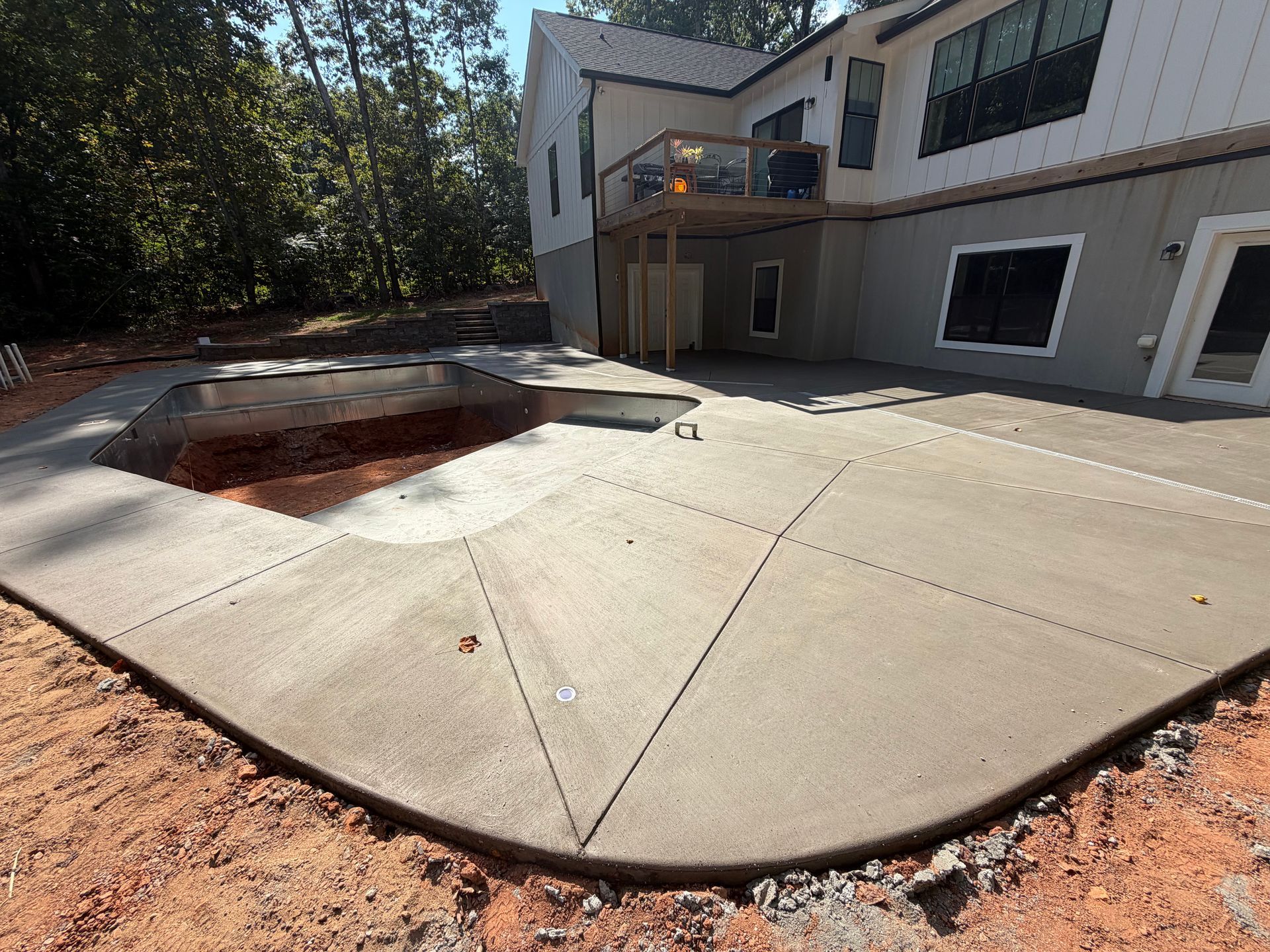 Newly poured concrete patio beside a modern house with a deck.