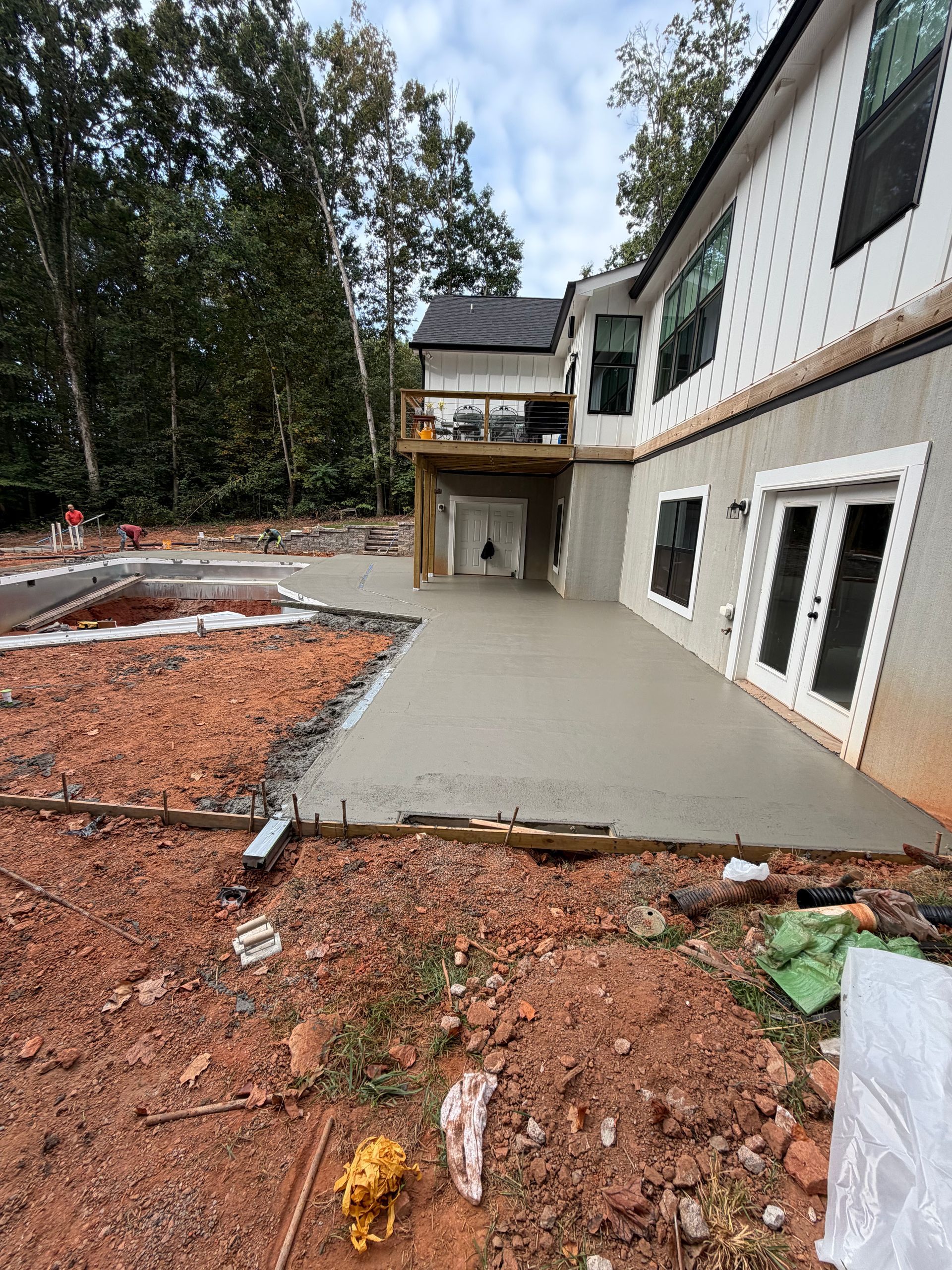 Newly poured concrete patio beside a house under construction; exposed red earth and trees surround.