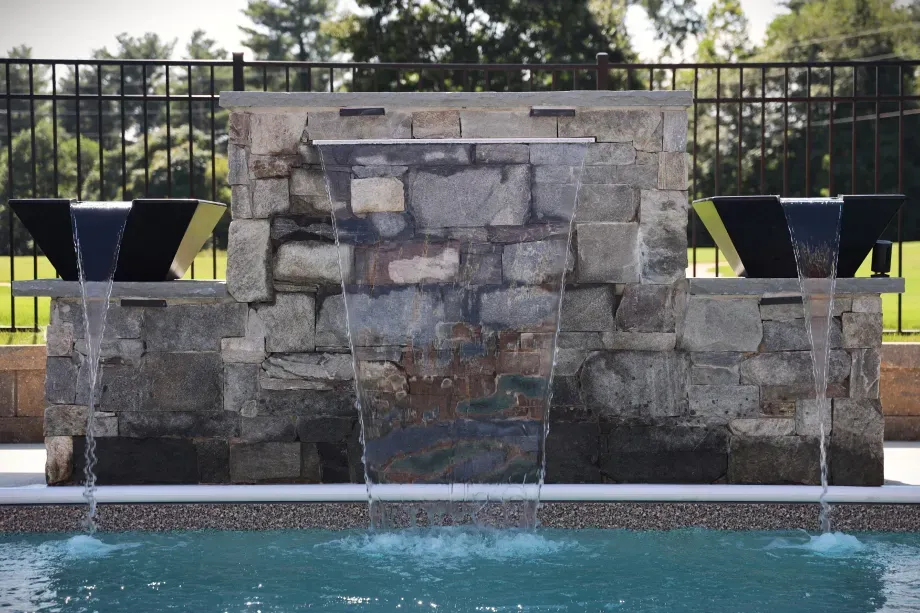 Stone water feature with three waterfalls cascading into a pool.