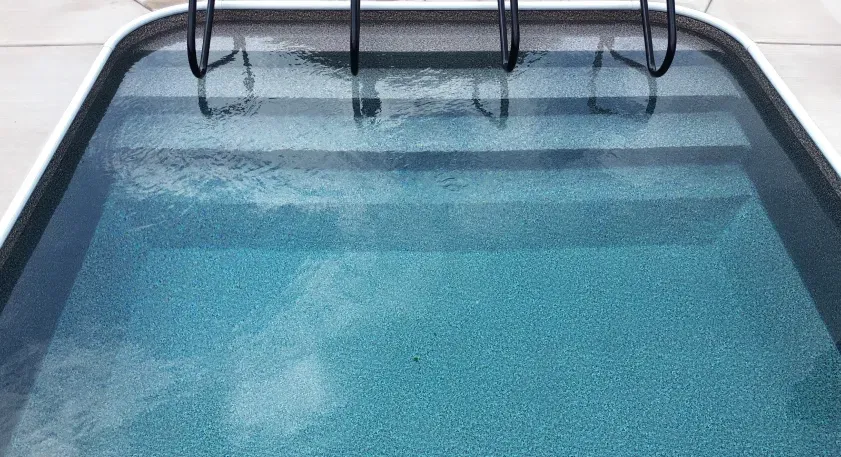 Pool with water and steps, black handrail. Blue water, white border.