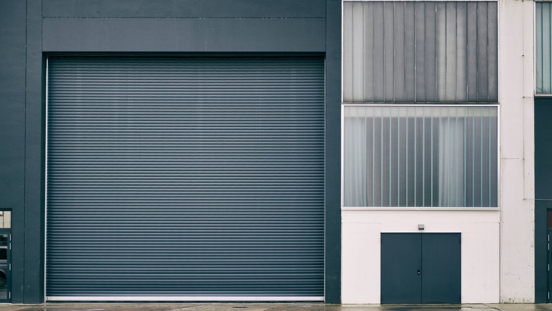 A black, four-section garage door with small windows at the top, set in a stone facade with a concrete driveway.
