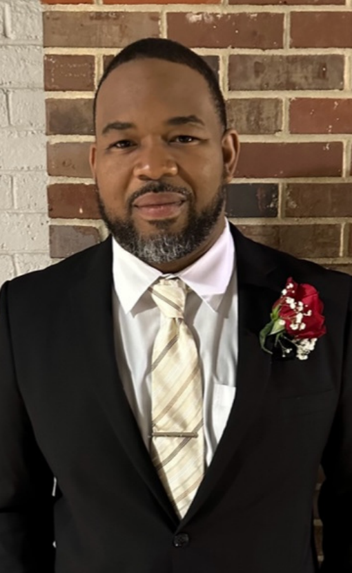 a man in a suit and tie is standing in front of a brick wall .