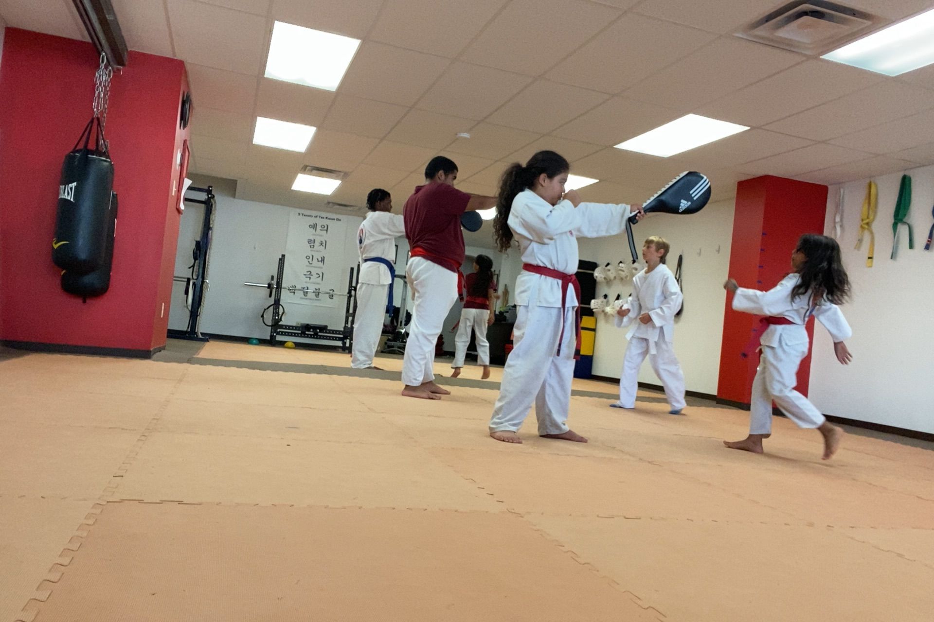 People in white karate uniforms practicing kicks in a dojo, with one person in focus.