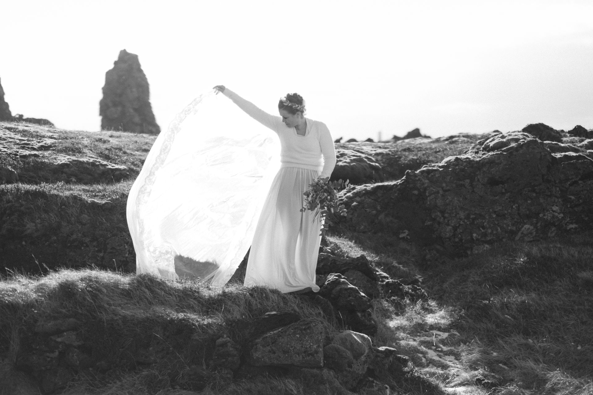 A woman in a white dress is standing on top of a rocky hill.