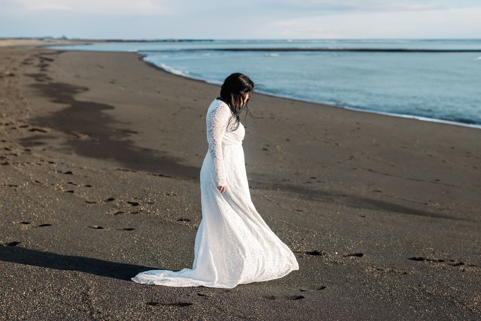 A woman in a white dress is walking on a beach.