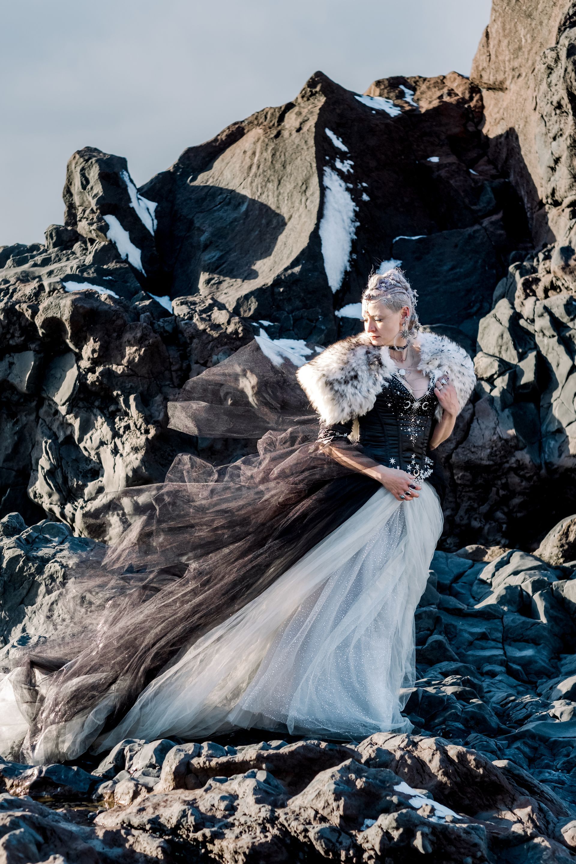 A woman in a black and white dress is standing on a rocky beach.