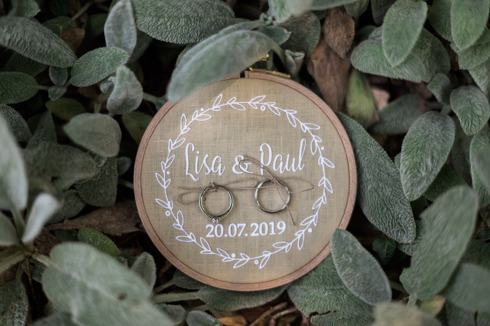 A pair of wedding rings sitting on top of a wooden ring holder surrounded by leaves.
