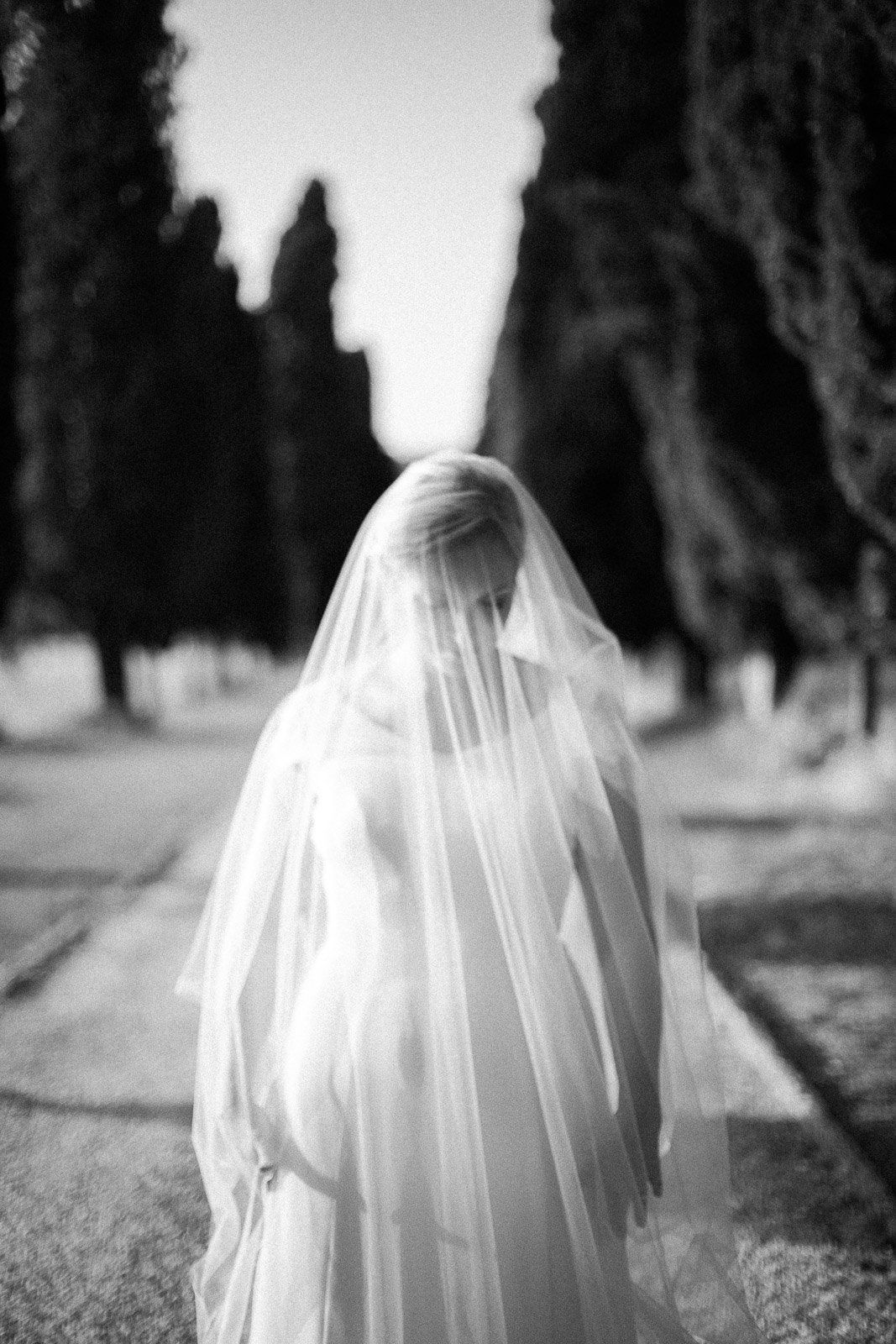 A bride in a wedding dress and veil is walking down a path.