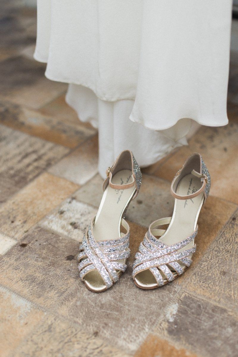 A pair of wedding shoes are sitting on a tiled floor next to a white dress.