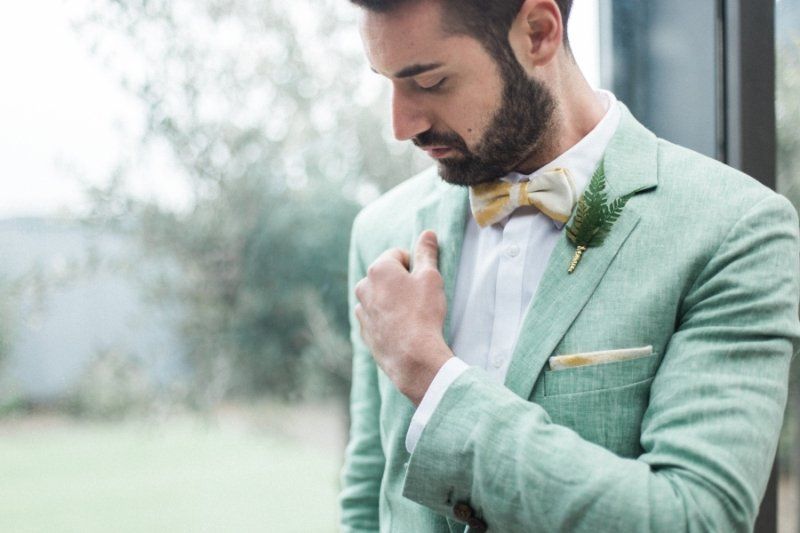 A man in a green suit and bow tie is adjusting his jacket.