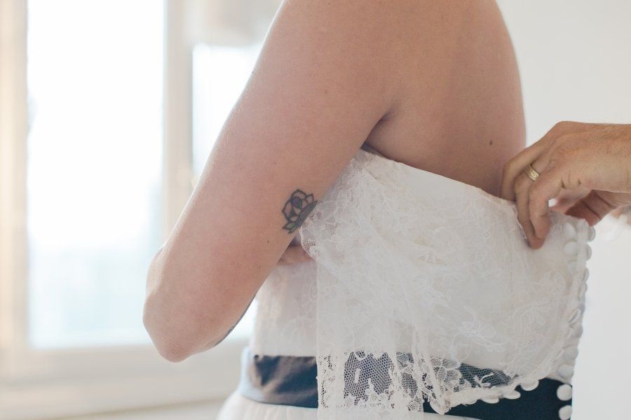 A woman with a tattoo on her arm is putting on a wedding dress.
