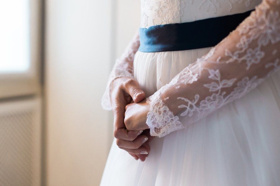 The bride is wearing a white lace dress with a blue sash around her waist.