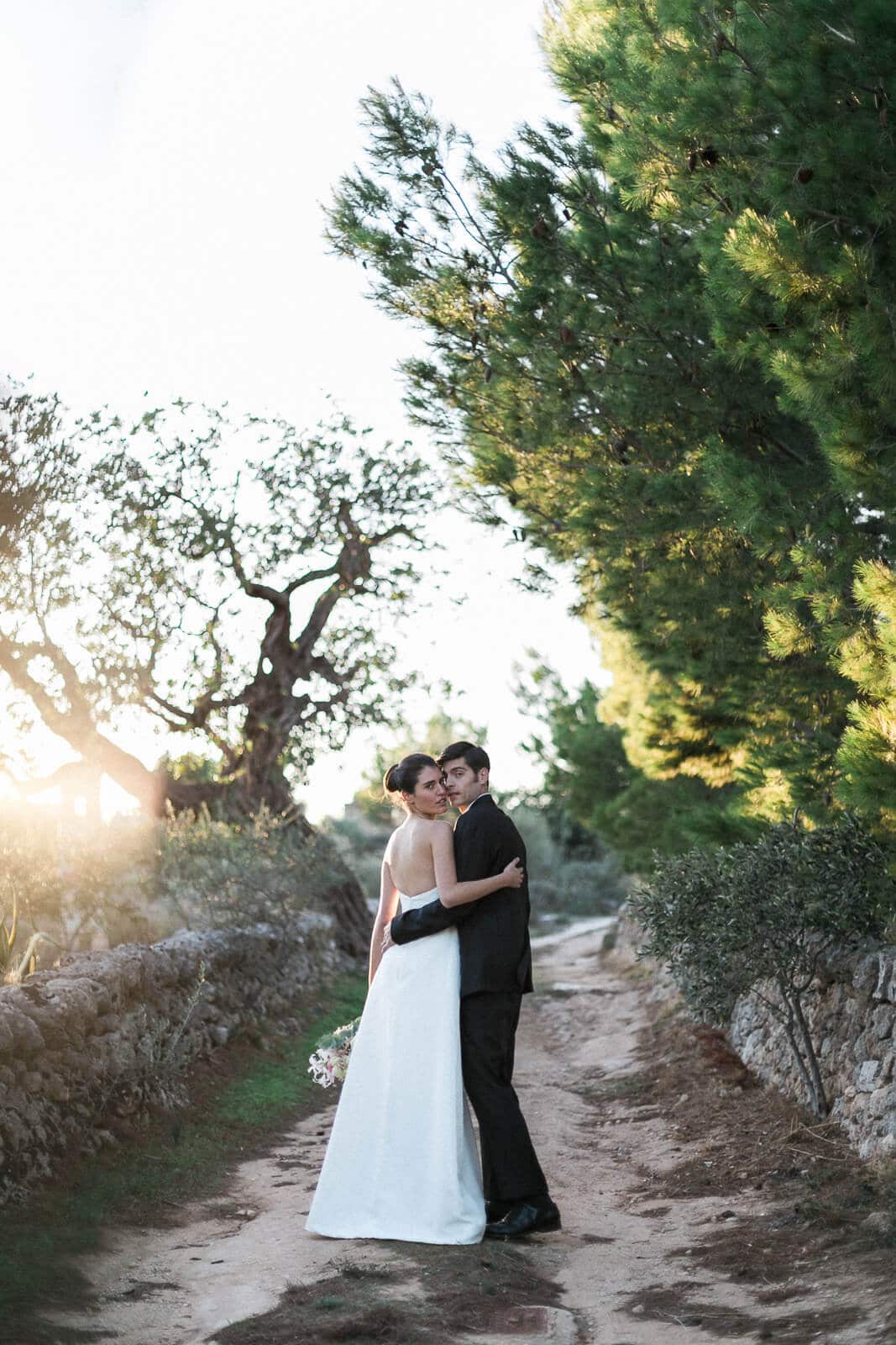 A bride and groom are standing next to each other on a dirt road.