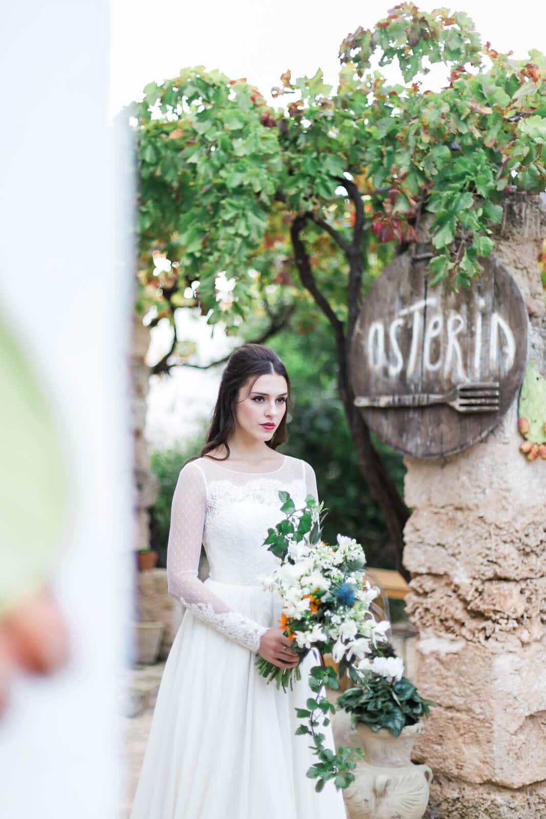 A bride in a white dress is holding a bouquet of flowers in front of a sign.