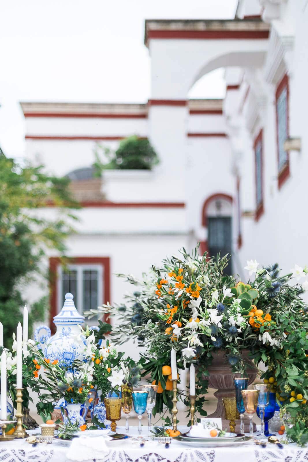 A table with flowers and candles on it in front of a white building.