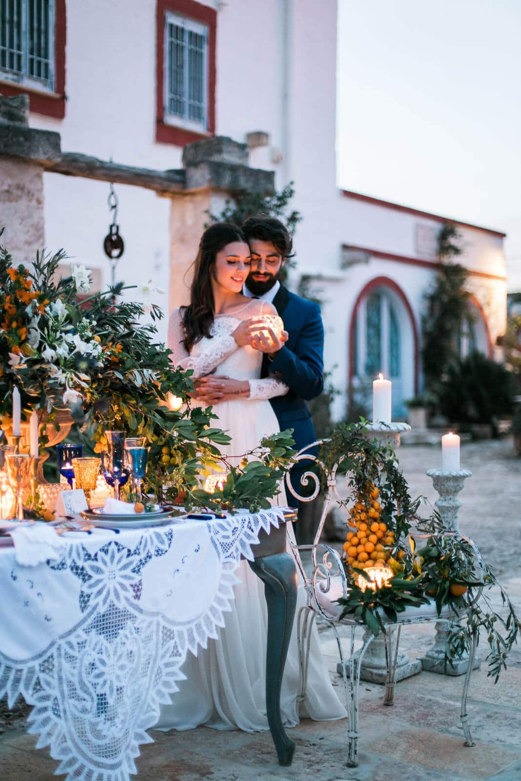 A bride and groom are sitting at a table with candles and flowers.