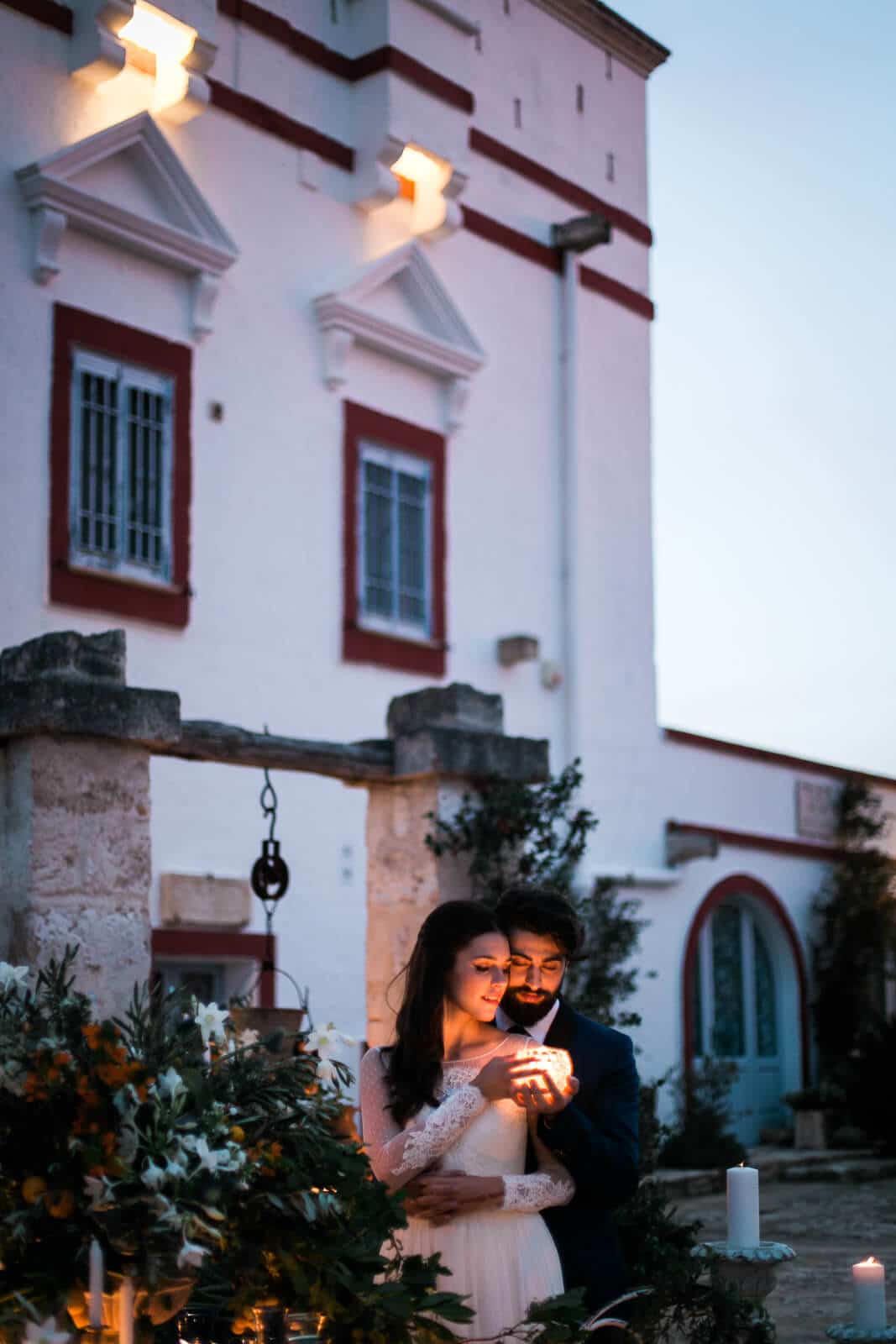 A bride and groom are holding a candle in front of a building.