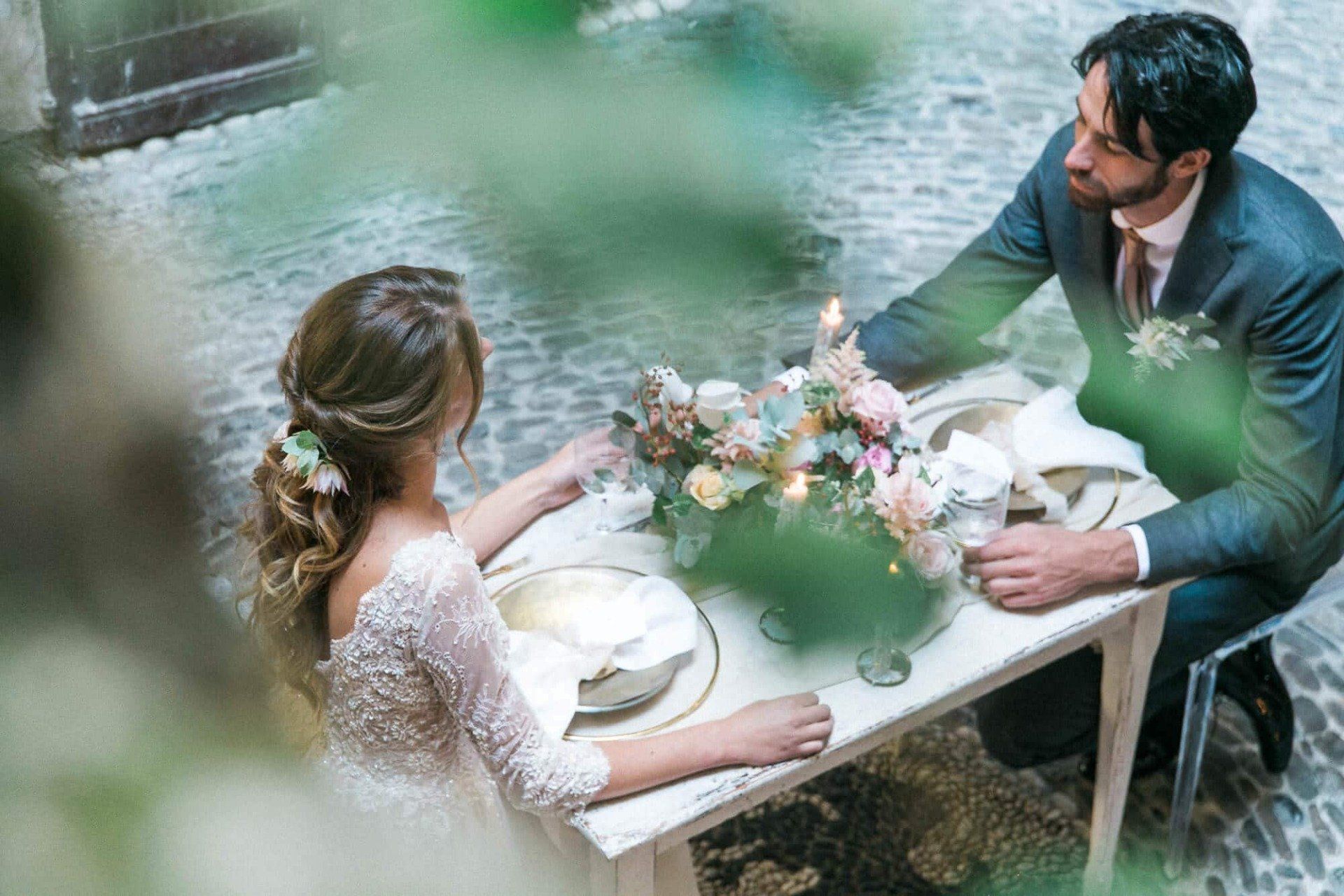 A bride and groom are sitting at a table with flowers on it.