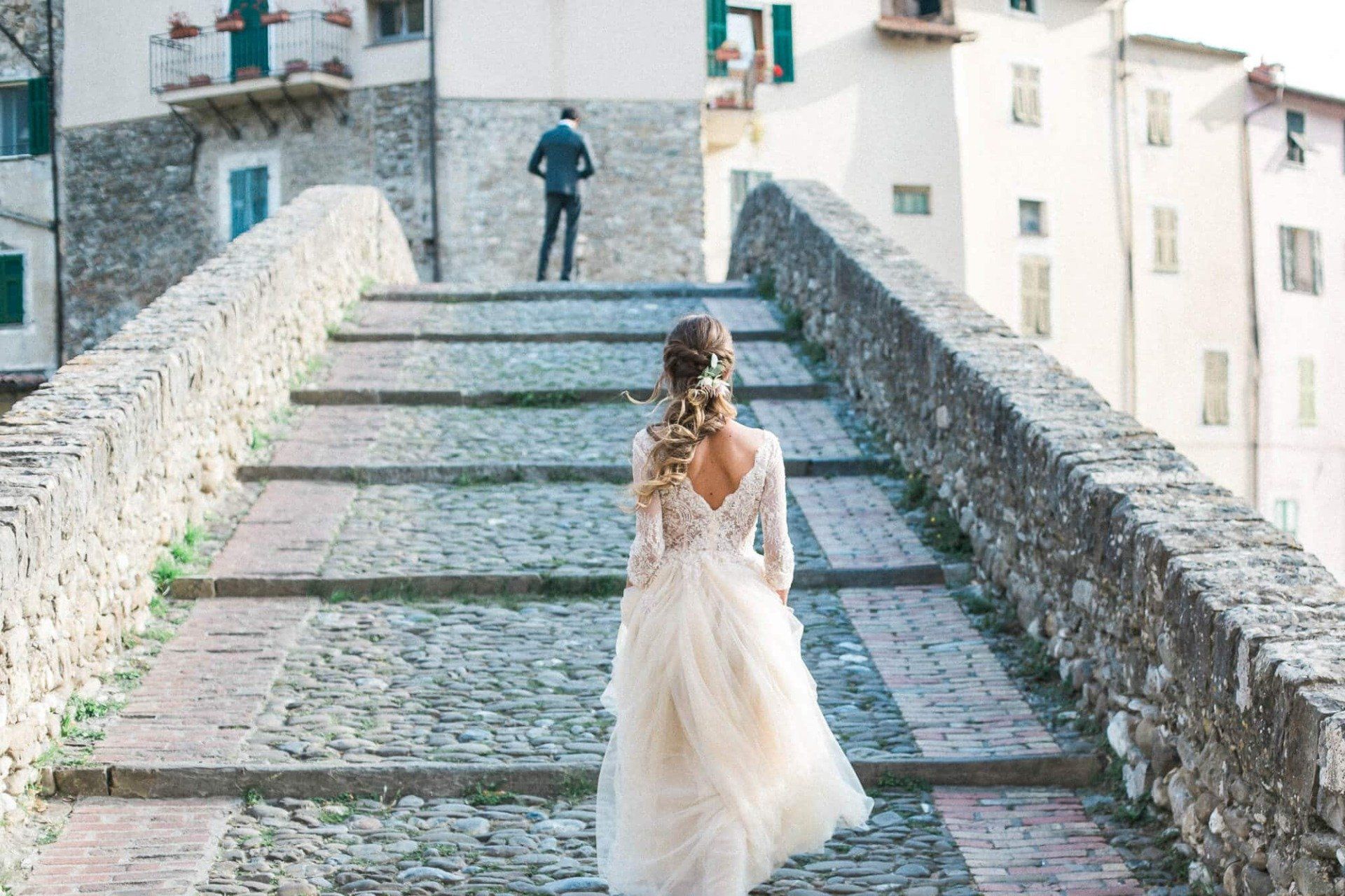 A bride and groom are walking across a stone bridge.