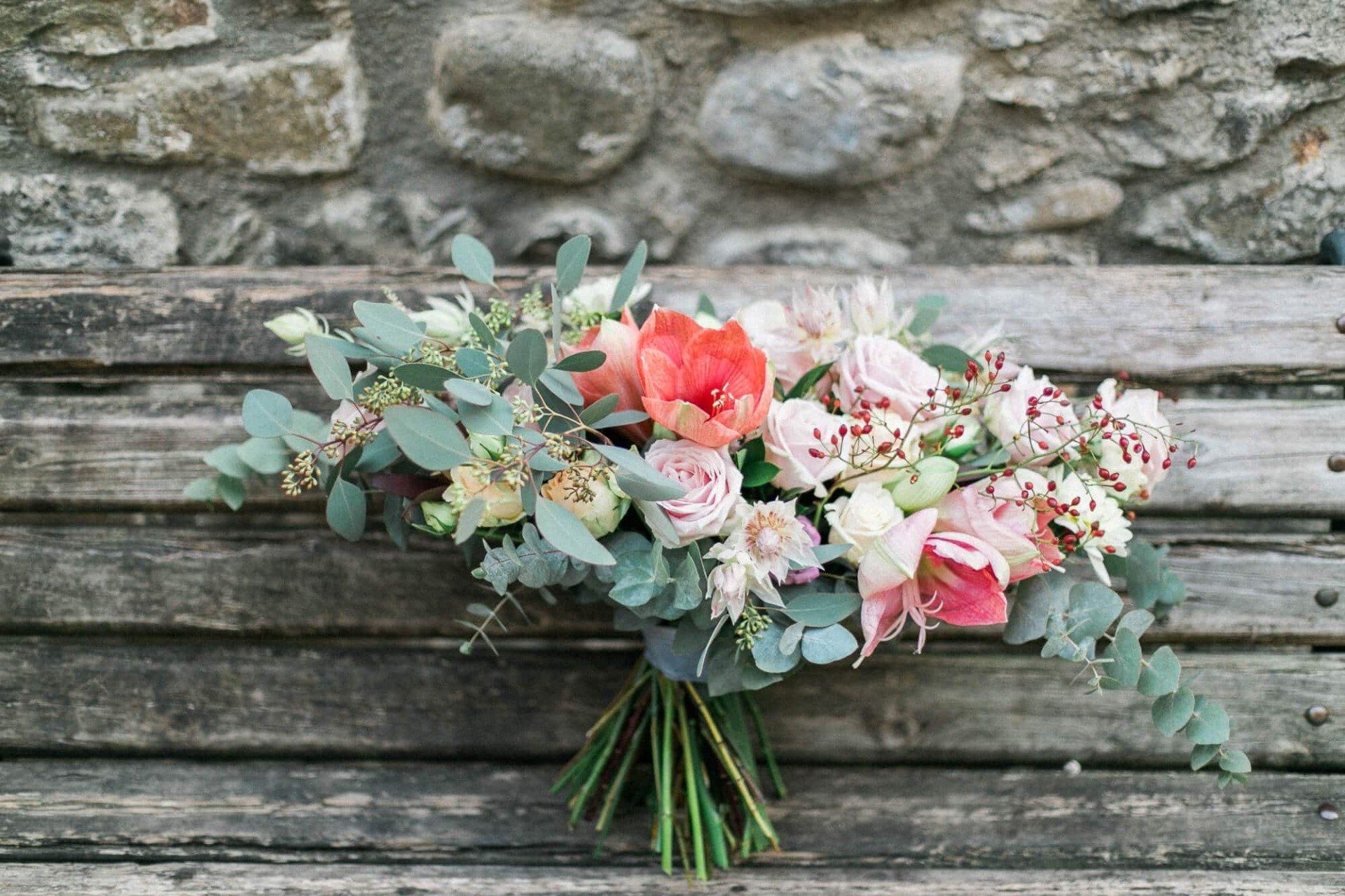 A bouquet of flowers is sitting on a wooden bench in front of a stone wall.