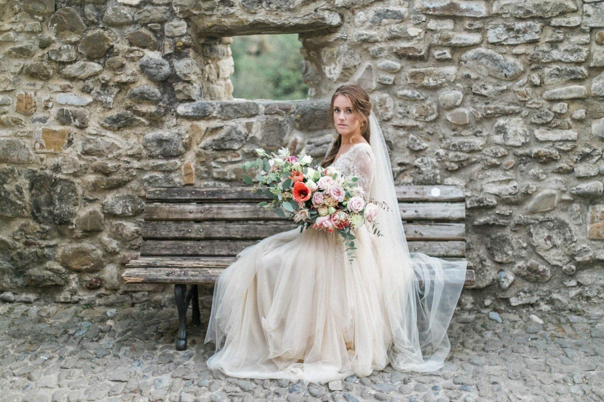 A bride in a wedding dress is sitting on a bench holding a bouquet of flowers.
